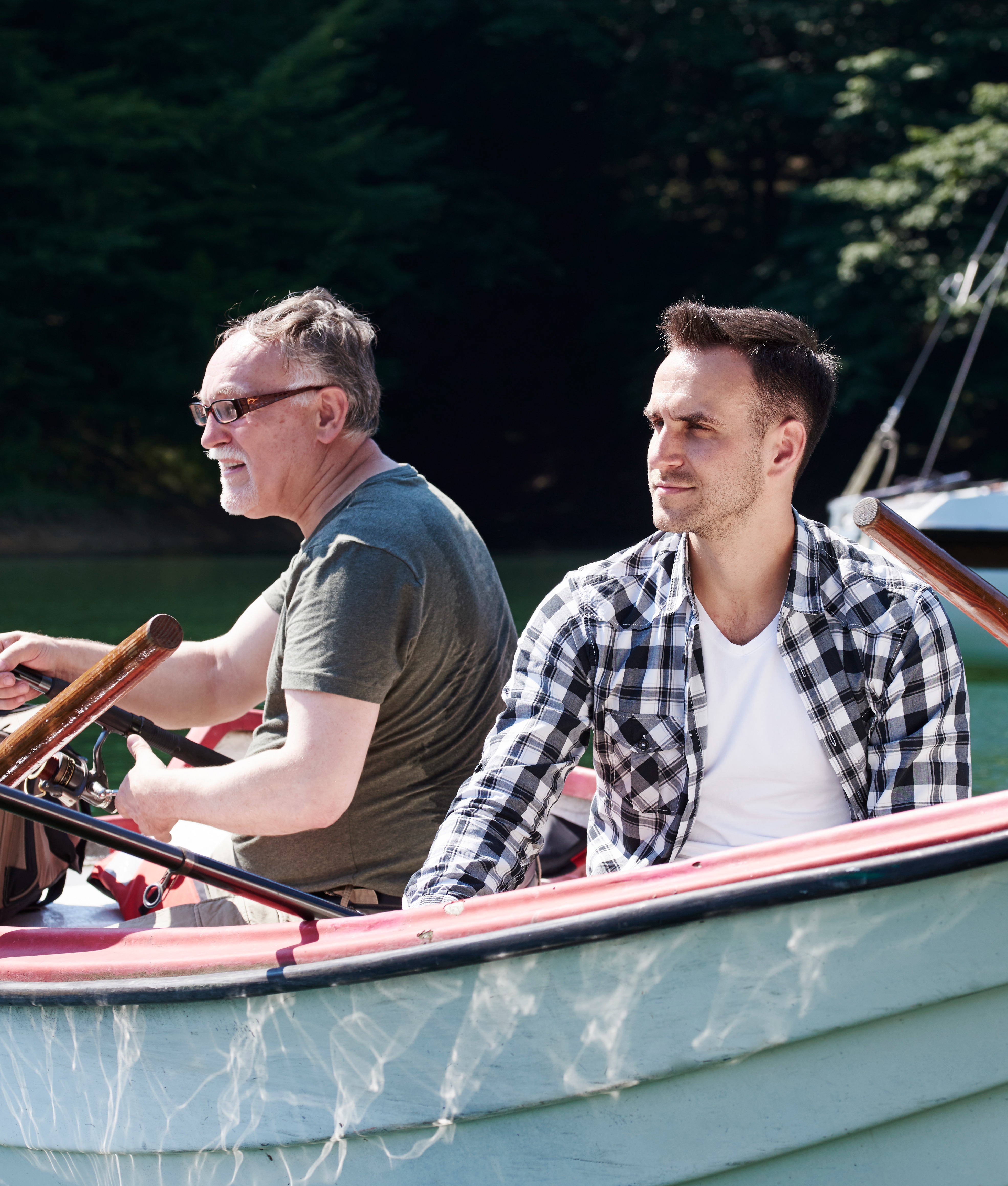 Men fishing together in a boat on a sunny day surrounded by lush nature.