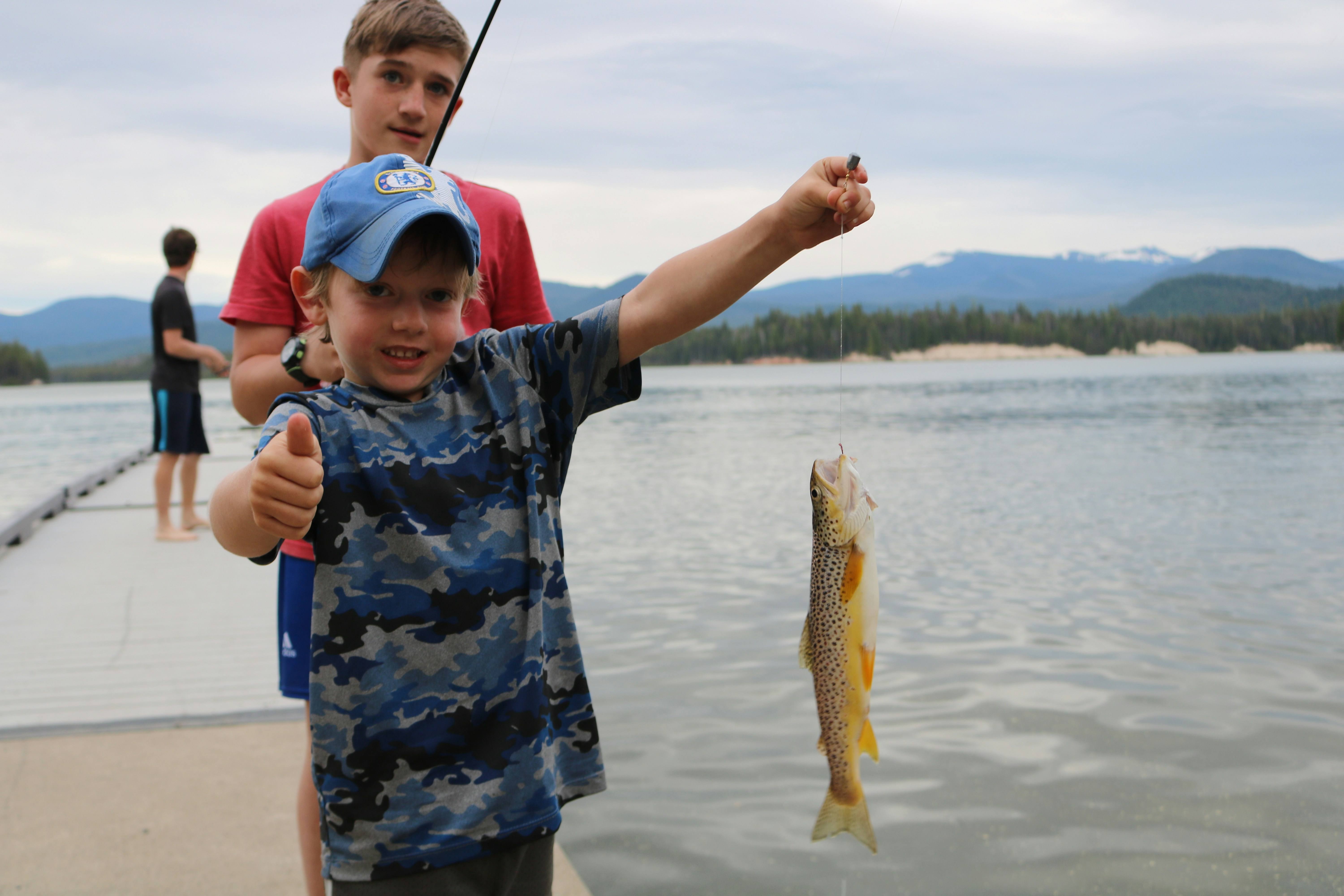 Young boy proudly holds a brown trout while fishing at a serene lakeside.