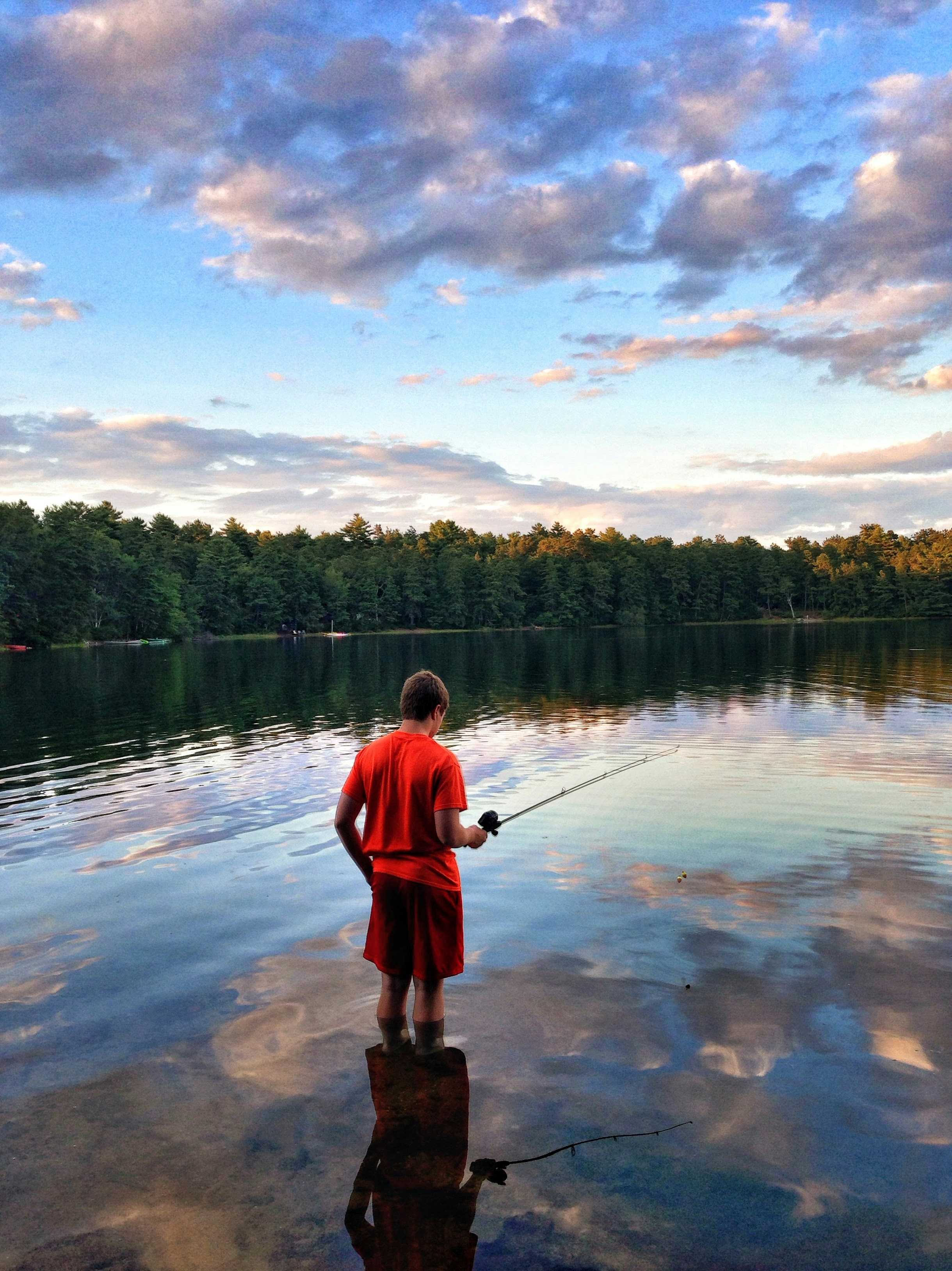 Young boy fishing at a serene lakeside, enjoying summer outdoors with fishing gear.