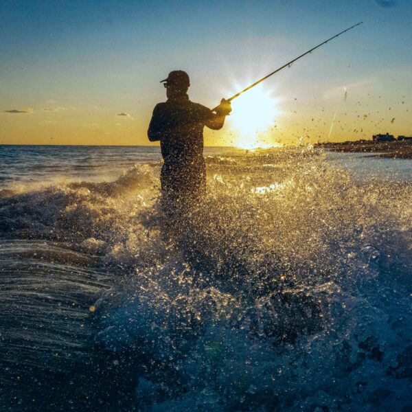 Fisherman casting a line at sunset, highlighting coastal fishing gear and ocean beauty.