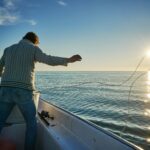 Fisherman casting line at sunrise on a serene fishing boat, showcasing peaceful angling moments.