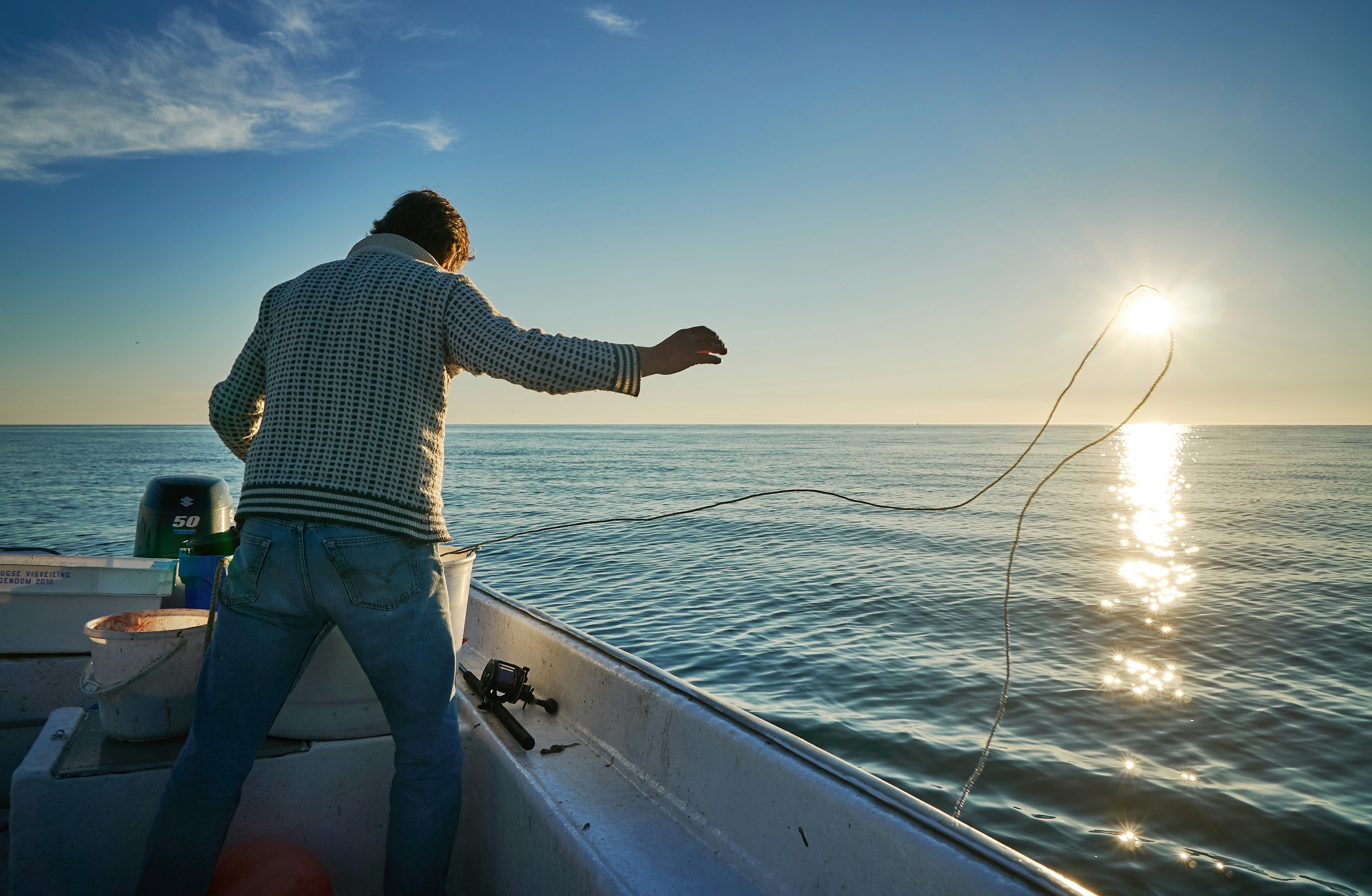 Fisherman casting line at sunrise on a serene fishing boat, showcasing peaceful angling moments.