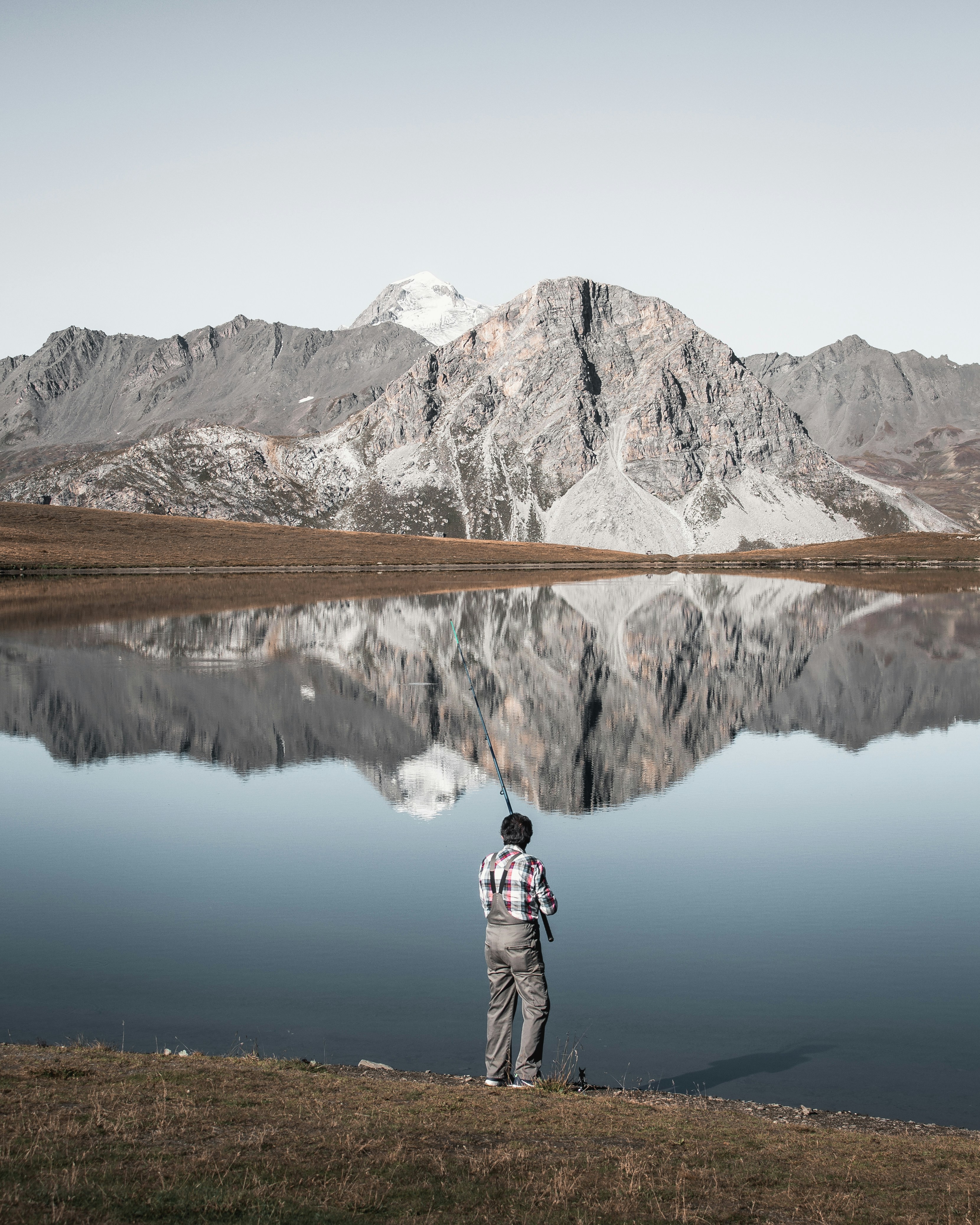 Fisherman enjoying tranquil lake fishing with mountains, perfect for outdoor adventure enthusiasts.