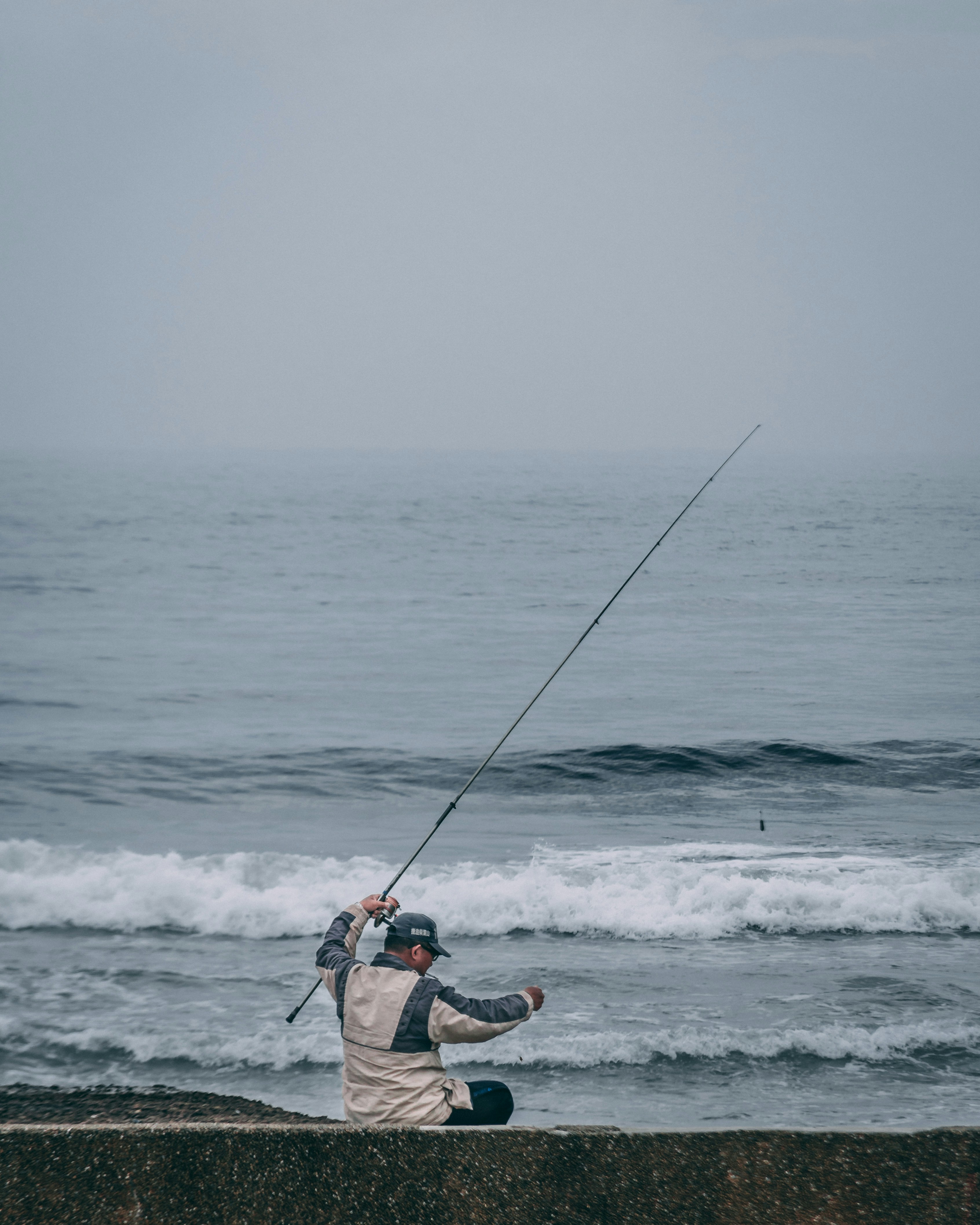 Fisherman casting line from coastal ledge in tranquil ocean setting, perfect for fishing enthusiasts.