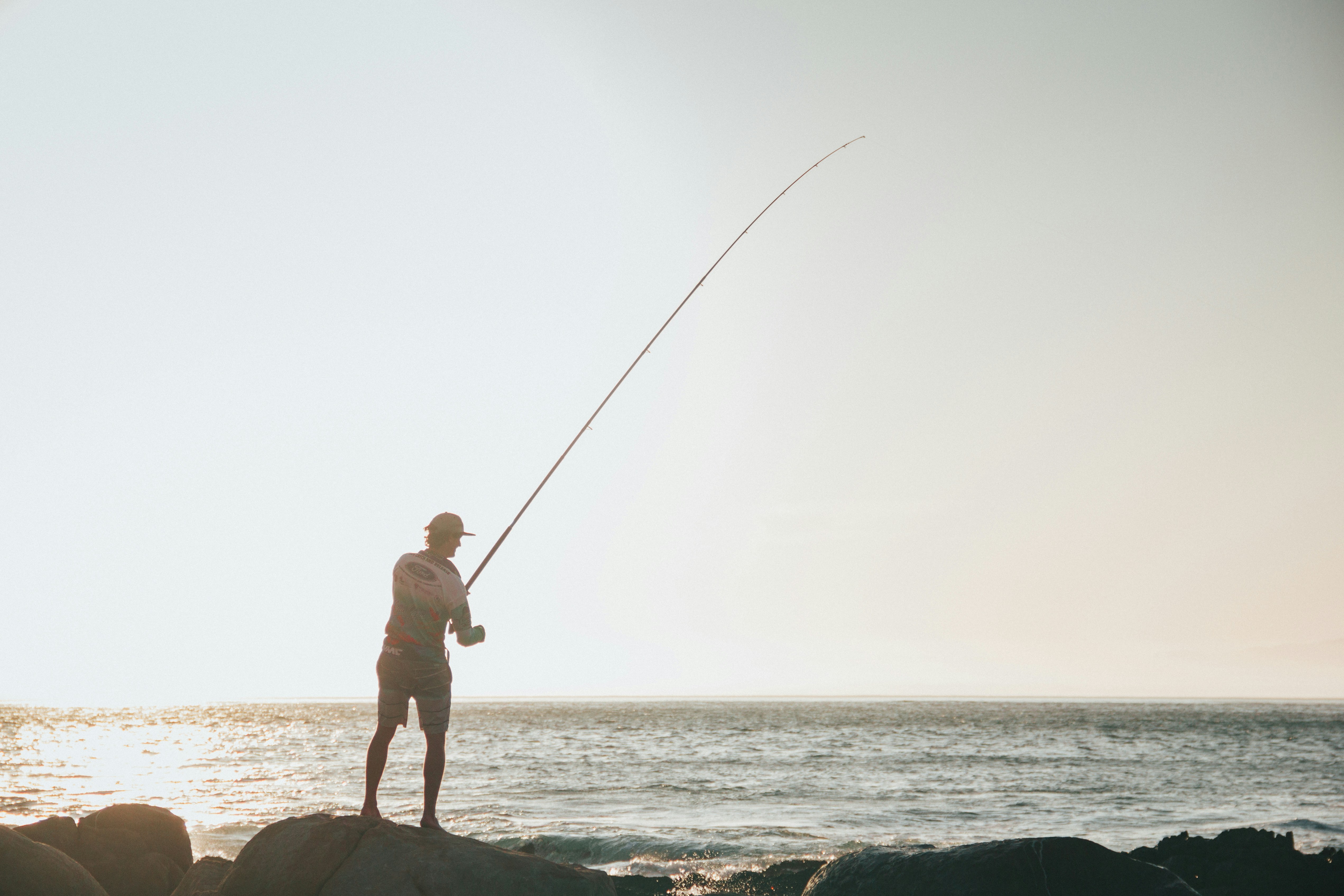 Fisherman casting a line at sunset, showcasing peaceful coastal fishing and outdoor lifestyle.