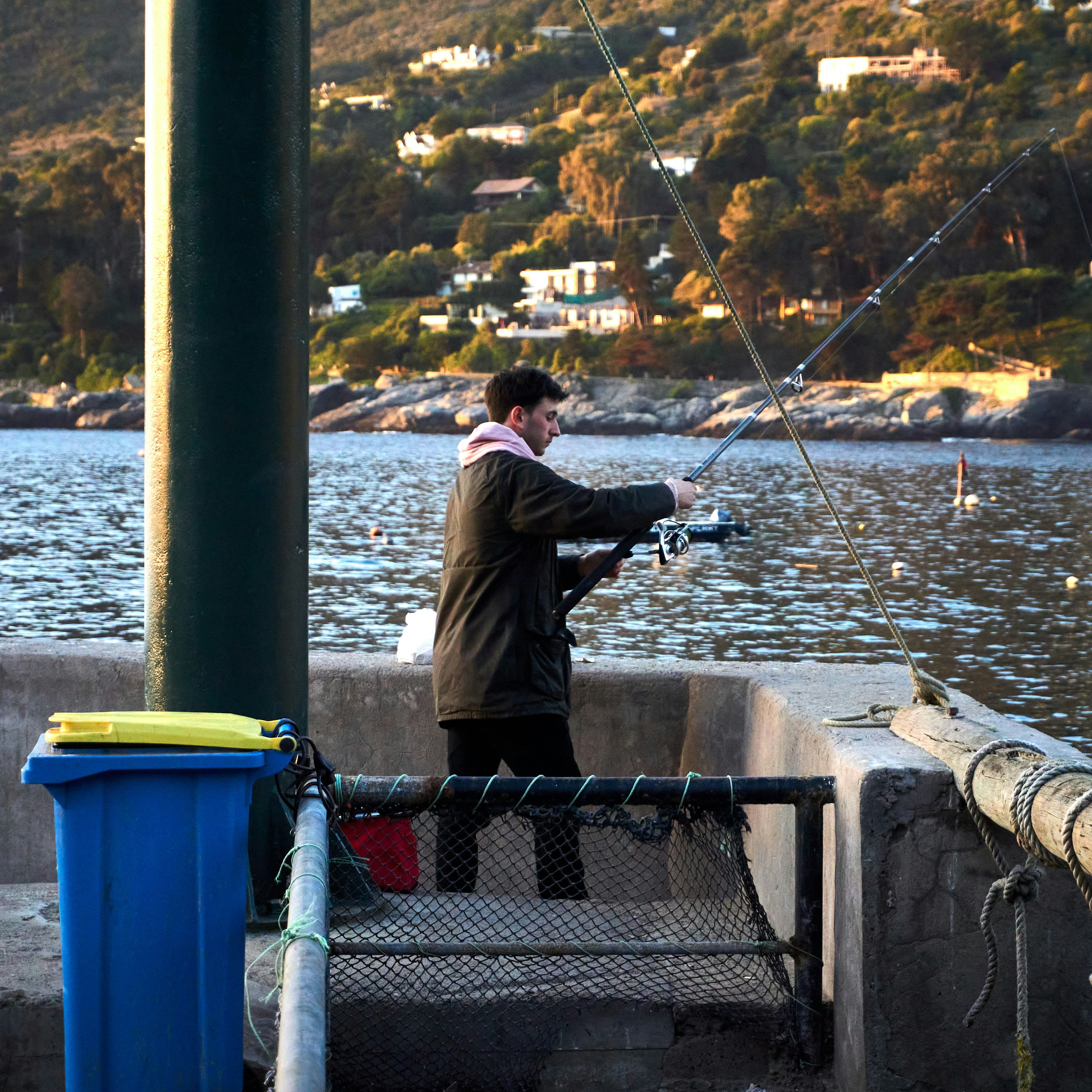 A young man fishing from a pier at sunset, enjoying the tranquil waterside experience.