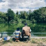 Grandfather and grandson enjoying fishing together by a peaceful lake under clear skies.