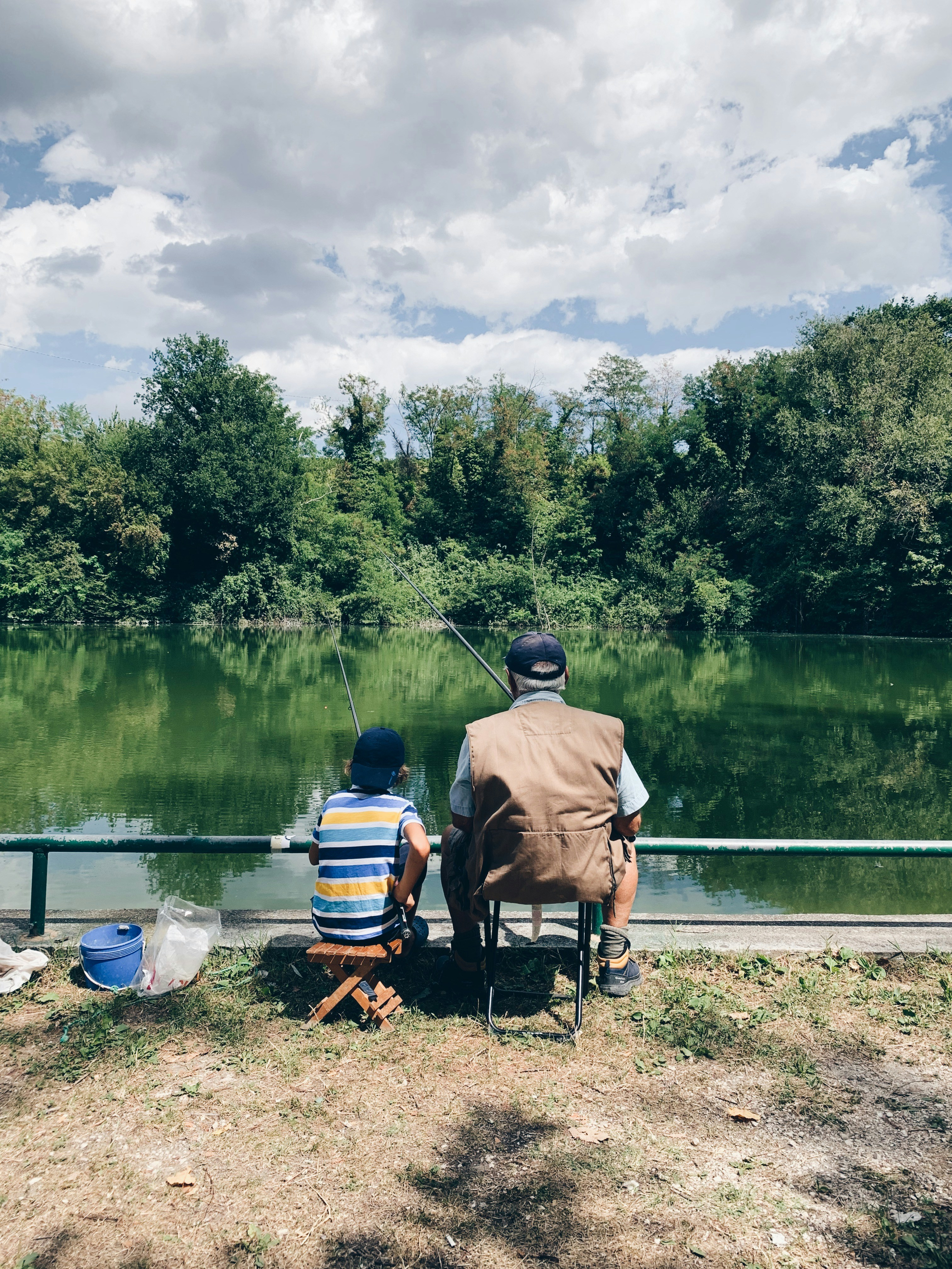 Grandfather and grandson enjoying fishing together by a peaceful lake under clear skies.