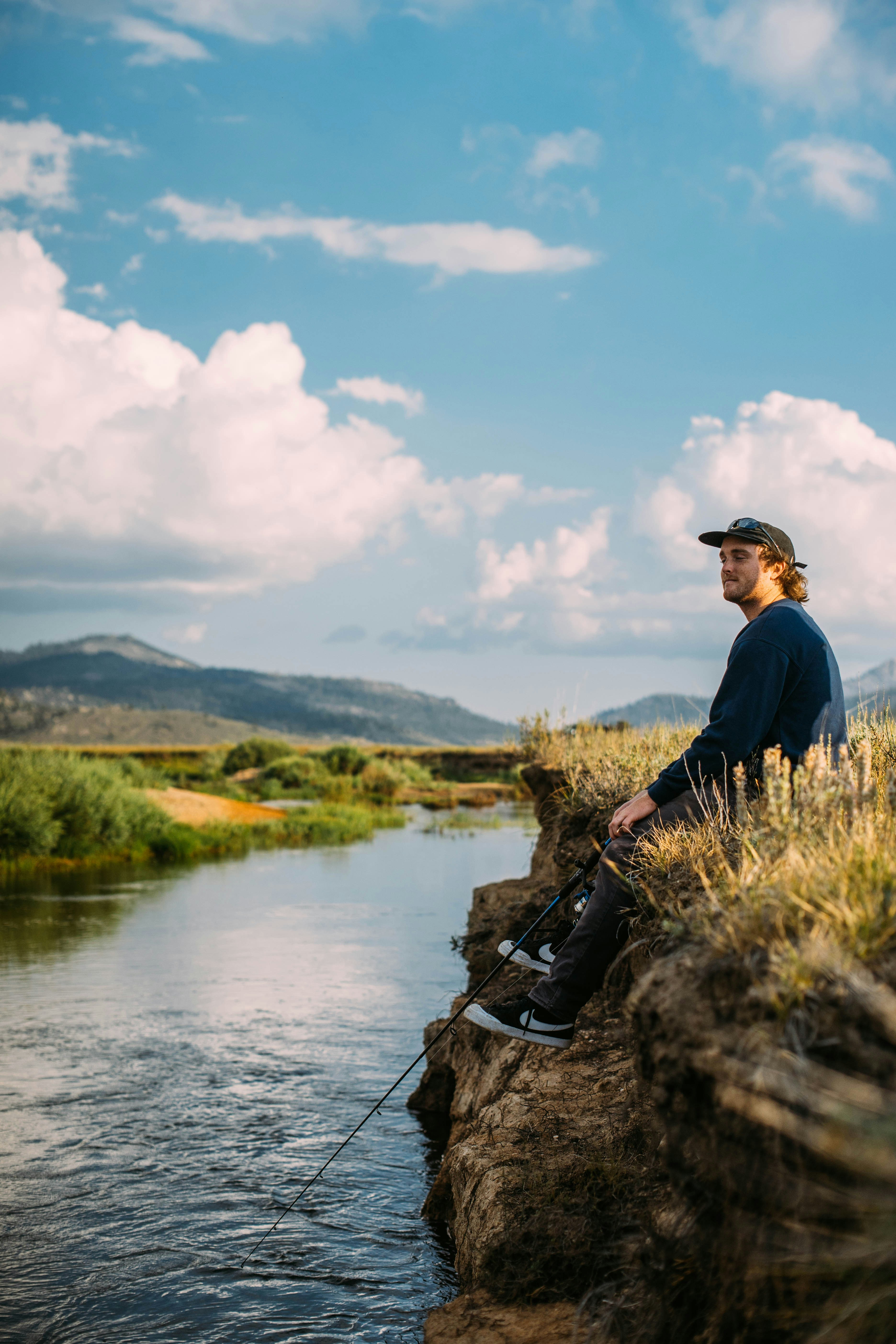 Young man fishing by a tranquil river, enjoying natures serenity and a peaceful day outdoors.