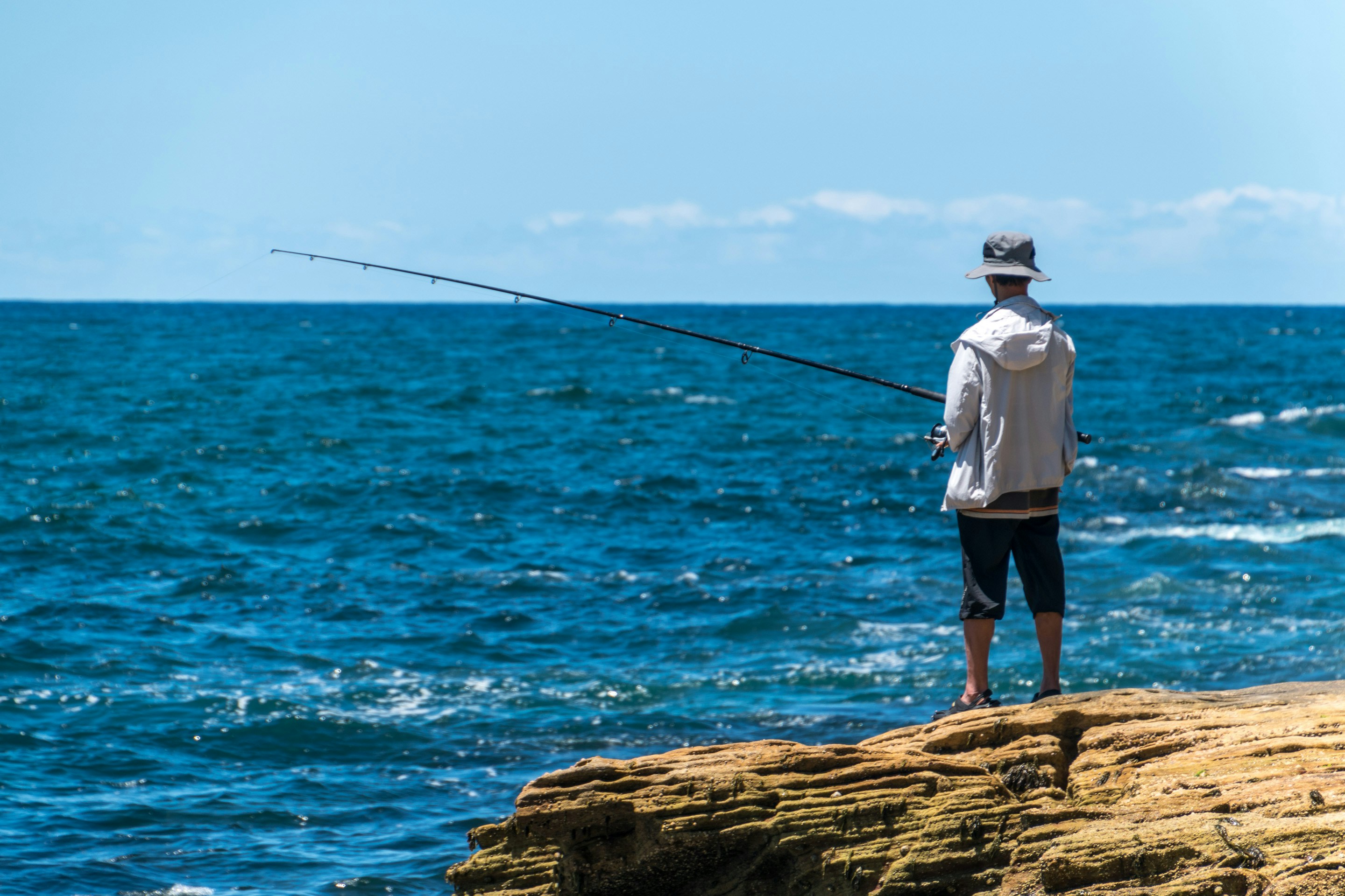 Angler fishing from a rocky shore, enjoying coastal serenity and beautiful ocean views.