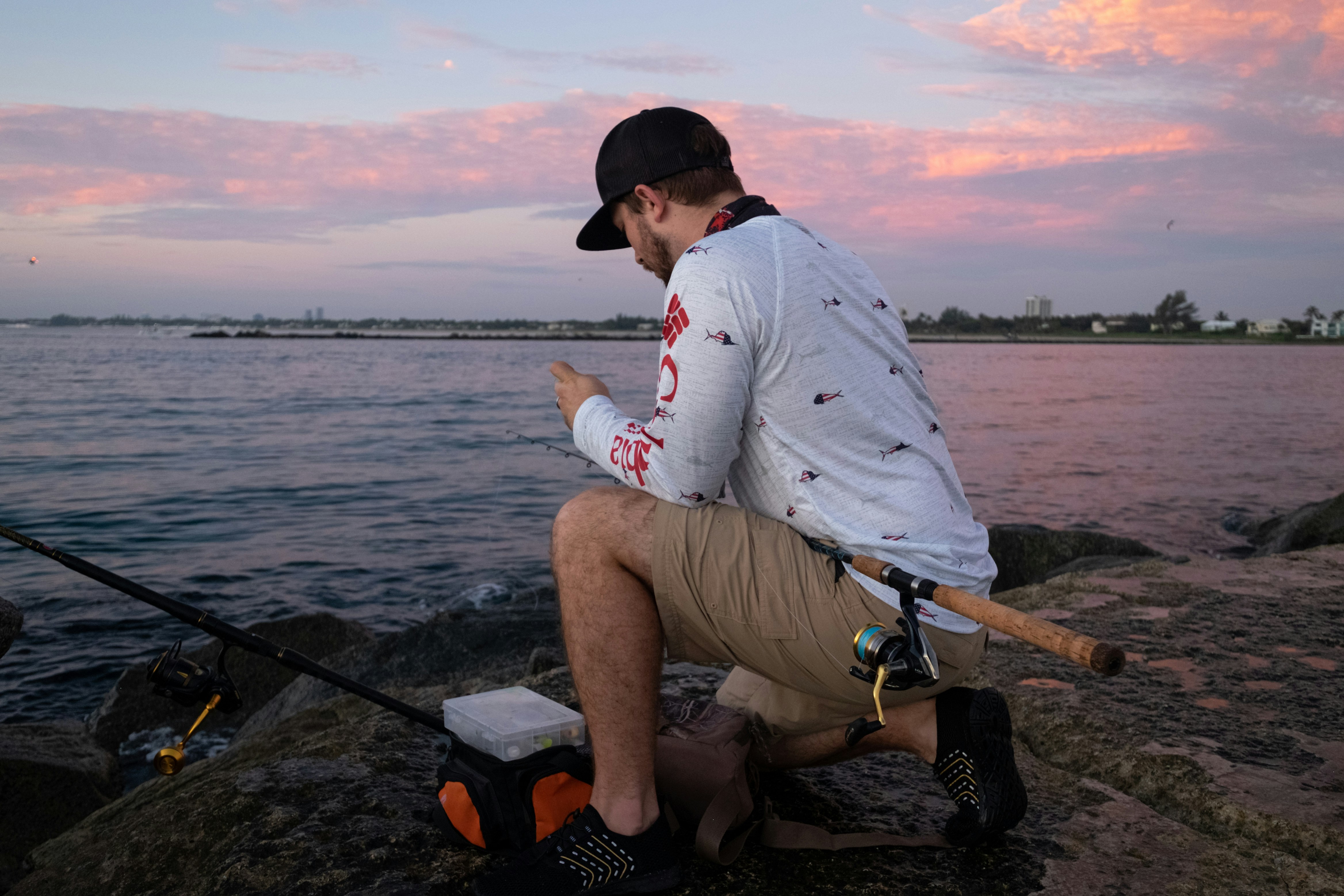 Man fishing on a rocky jetty at sunset, enjoying gear and mobile updates.