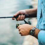 Person fishing by the water, showcasing quality fishing gear in a serene outdoor setting.