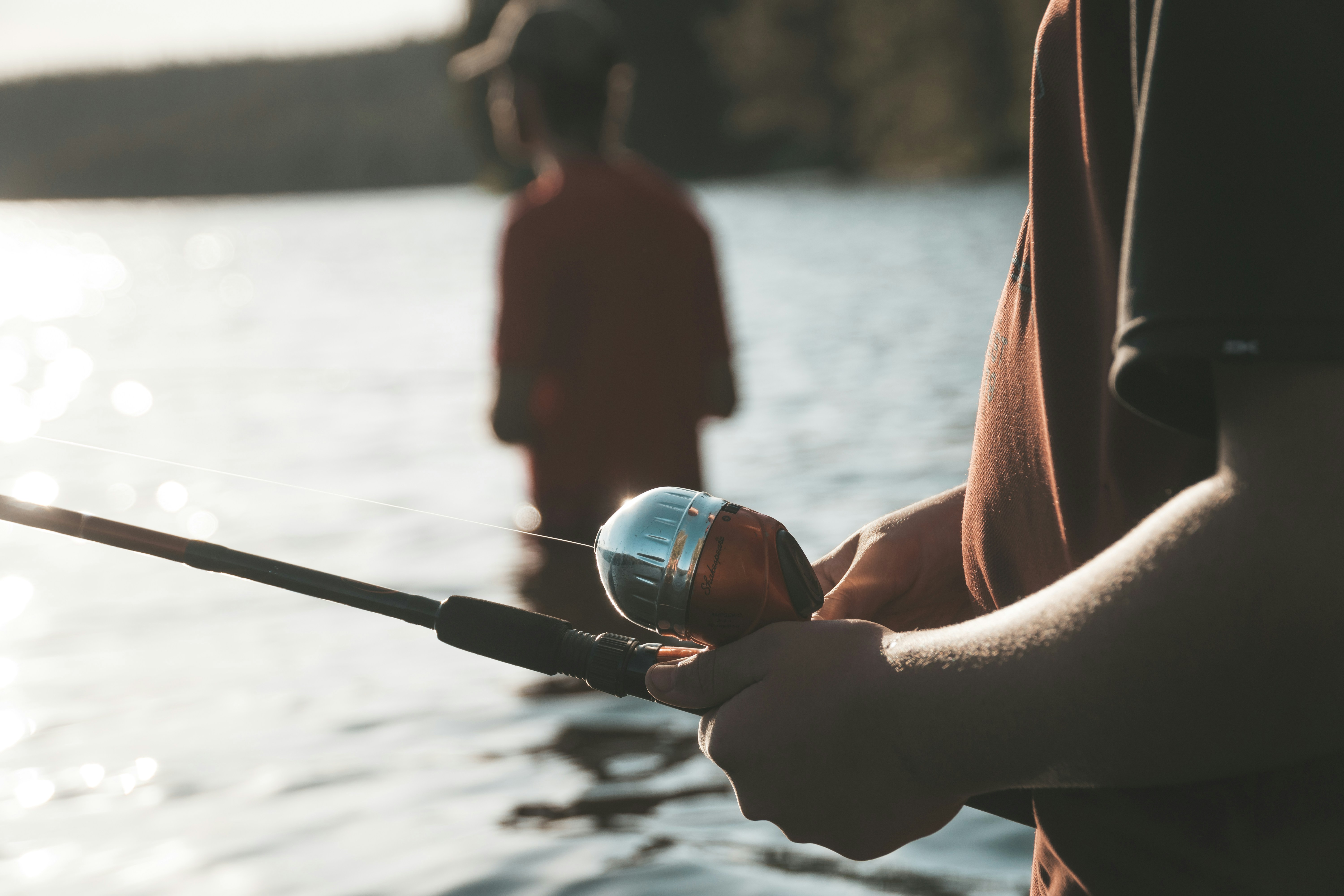 Two anglers fish peacefully by a serene lake, showcasing fishing gear in a natural setting.