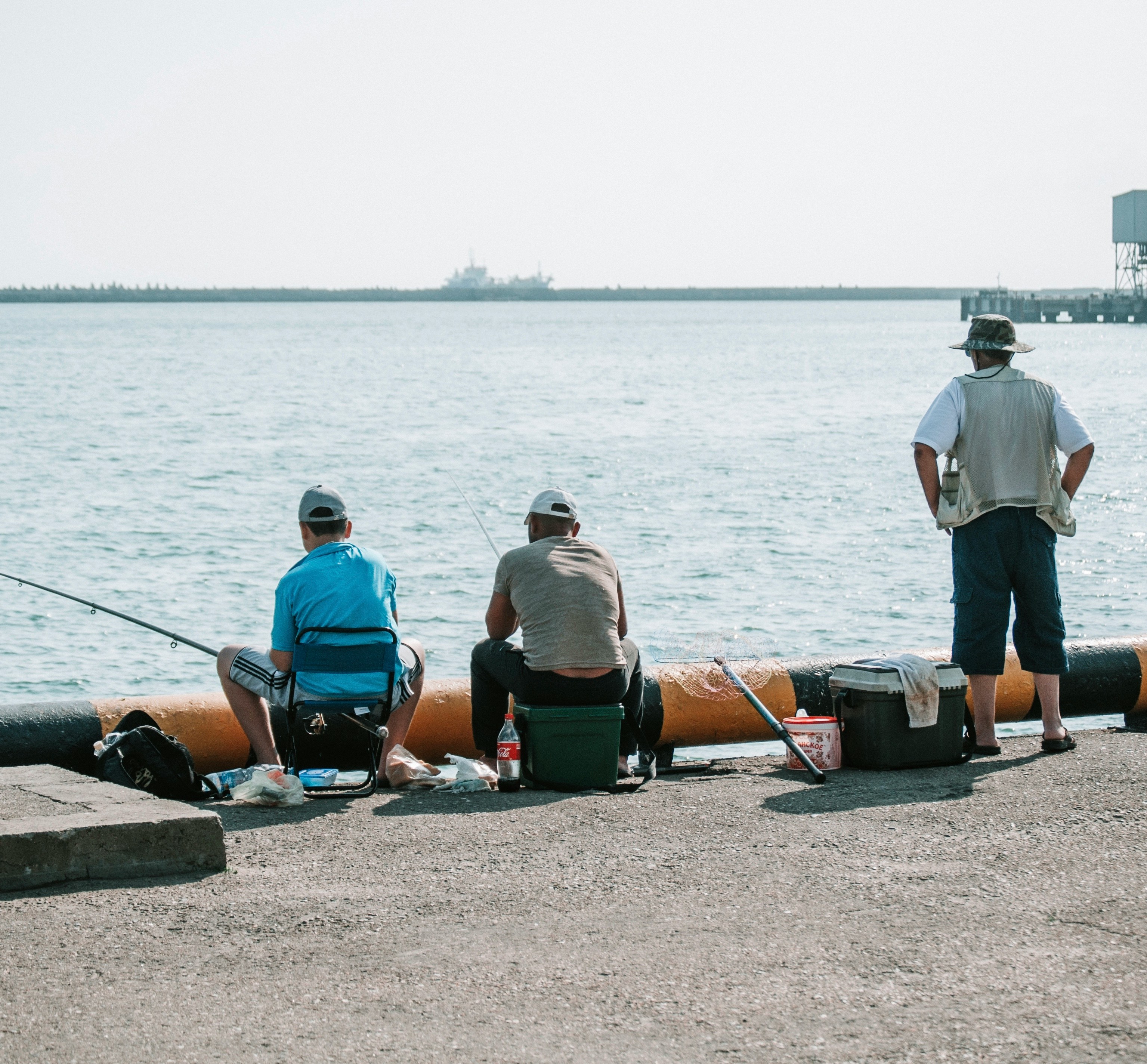 Three anglers enjoy a fishing day by the waterfront on a sunny day.