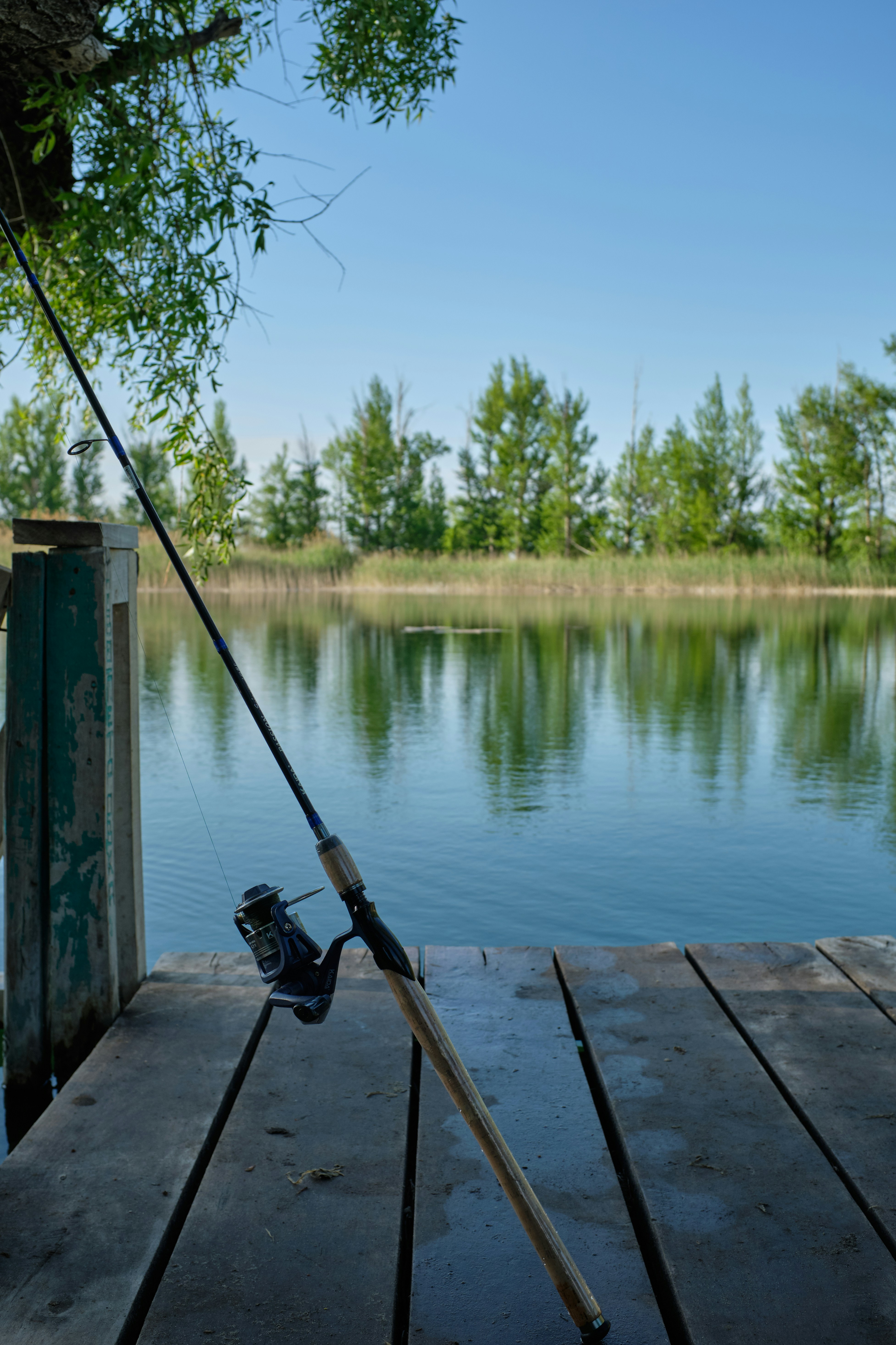 Serene fishing dock scene with rod and reel reflected in calm water, perfect for anglers.