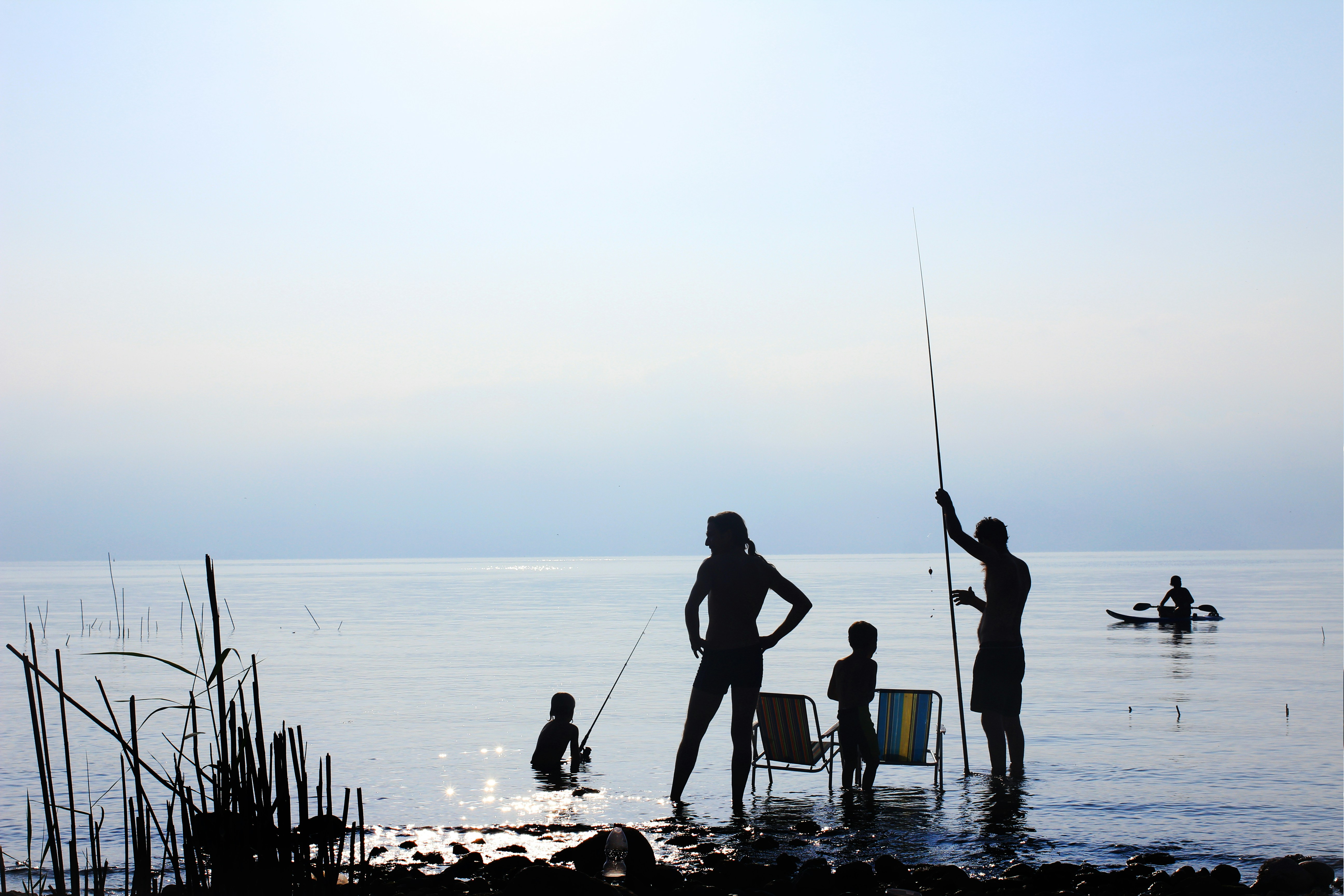 Family fishing at a tranquil lakeshore, enjoying nature with kids and kayaking adventures.