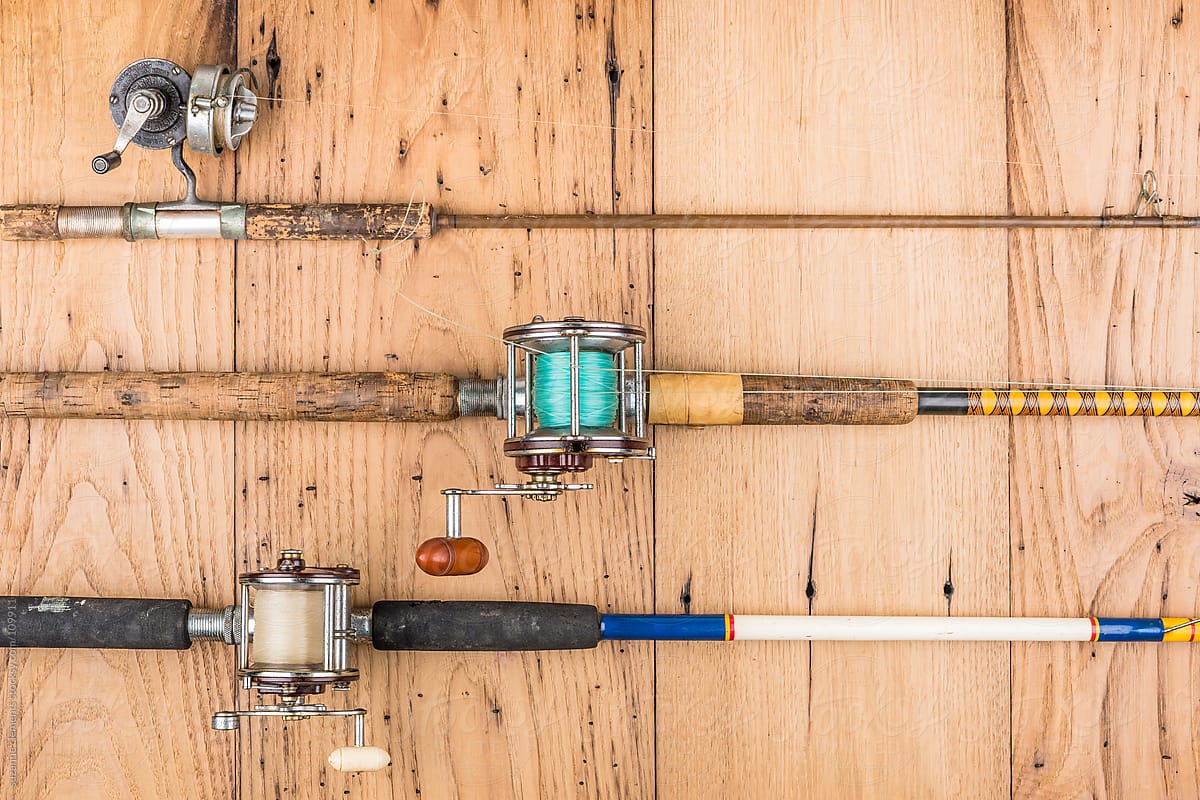 Vintage and modern fishing rods and reels displayed on rustic wood for anglers.