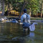 Angler in waders fishing peacefully by a picturesque river surrounded by nature.