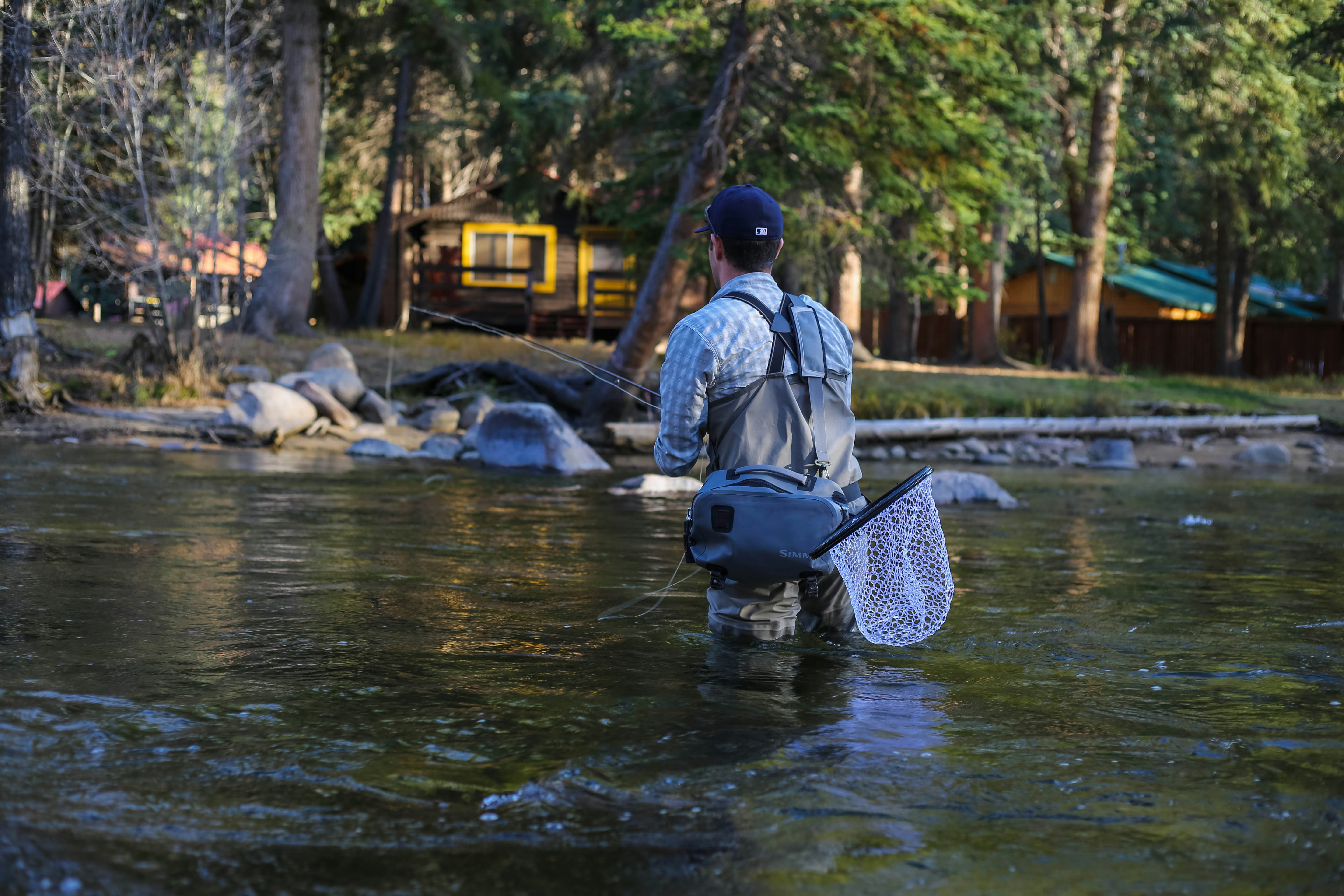 Angler in waders fishing peacefully by a picturesque river surrounded by nature.