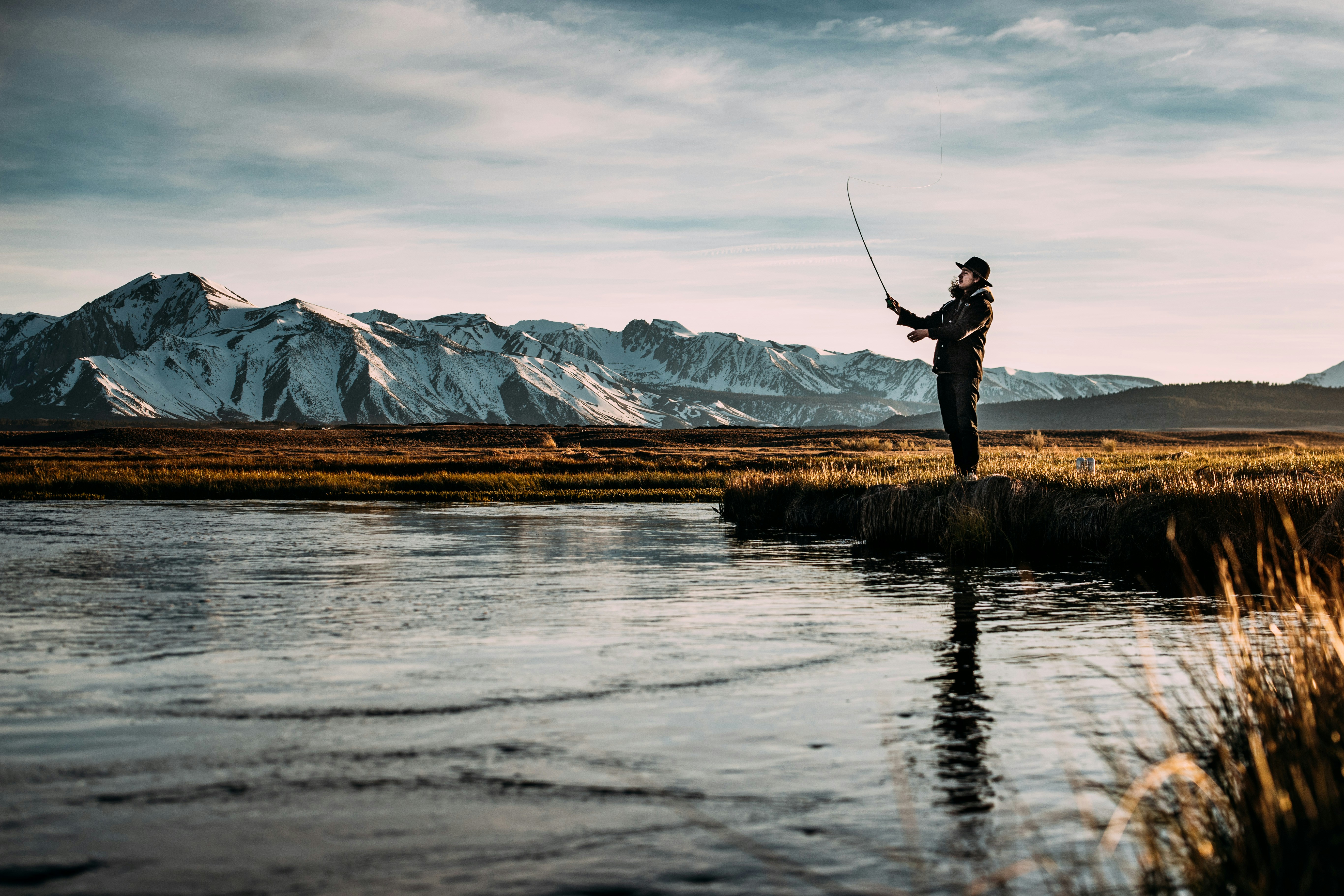 Angler fishing by serene river amidst stunning mountains, perfect for outdoor adventure enthusiasts.