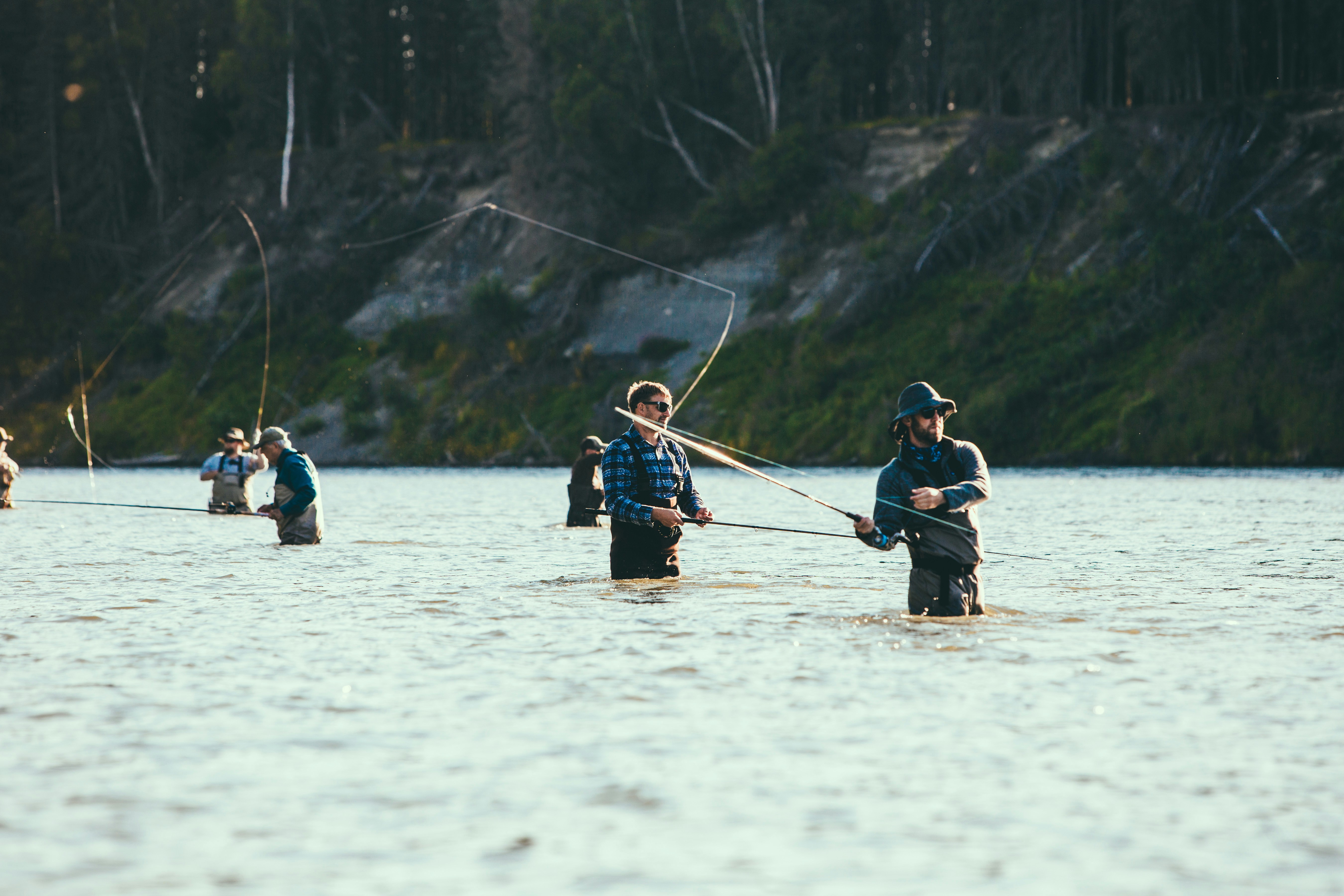 Fishermen in waders enjoy fly fishing in a picturesque, tranquil natural setting.