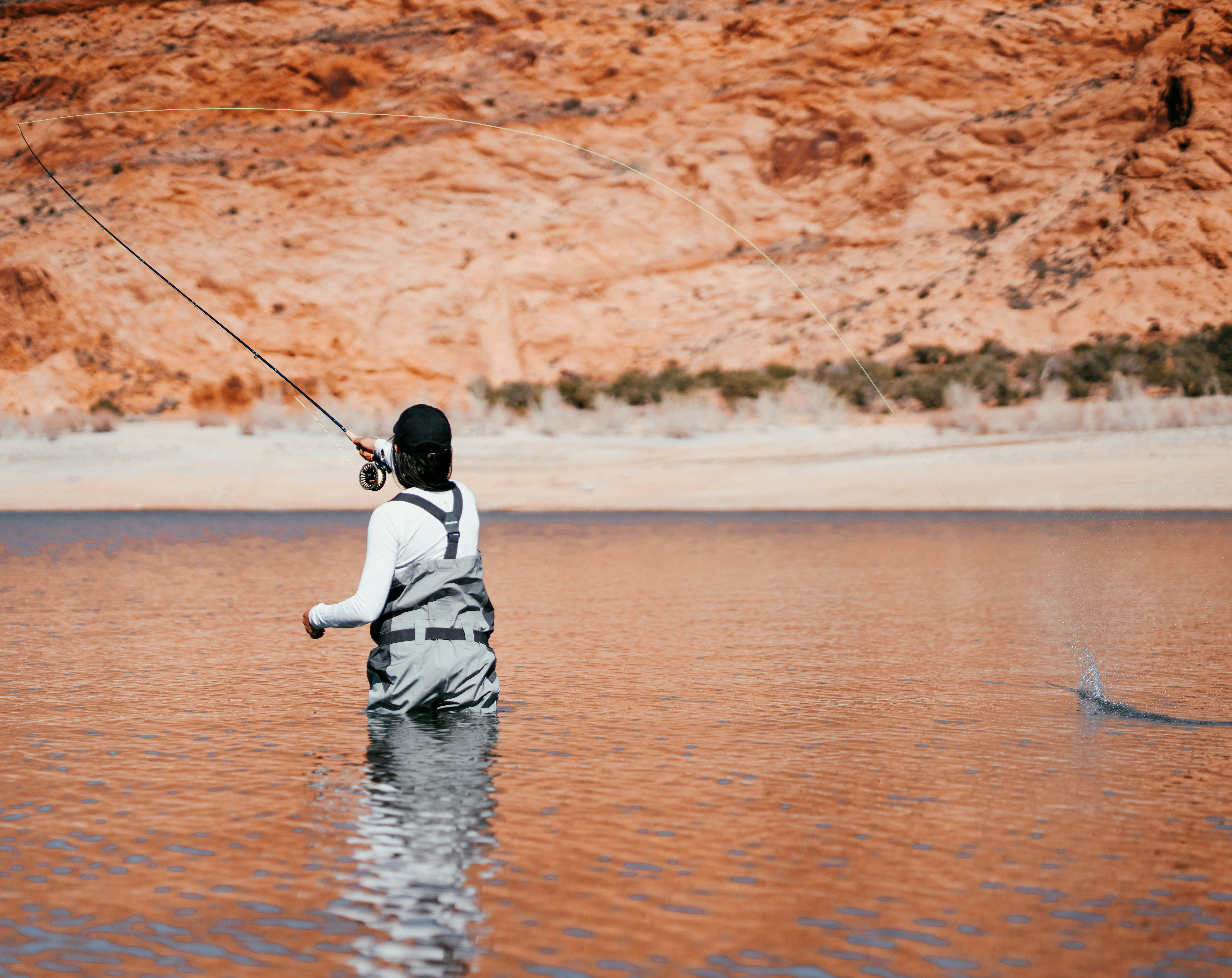 Angler fishing in tranquil lake surrounded by vibrant red rock formations and lush greenery.