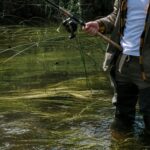 風光明媚な自然の風景のそばで、釣り道具を身に着けて浅瀬で釣りをする人。