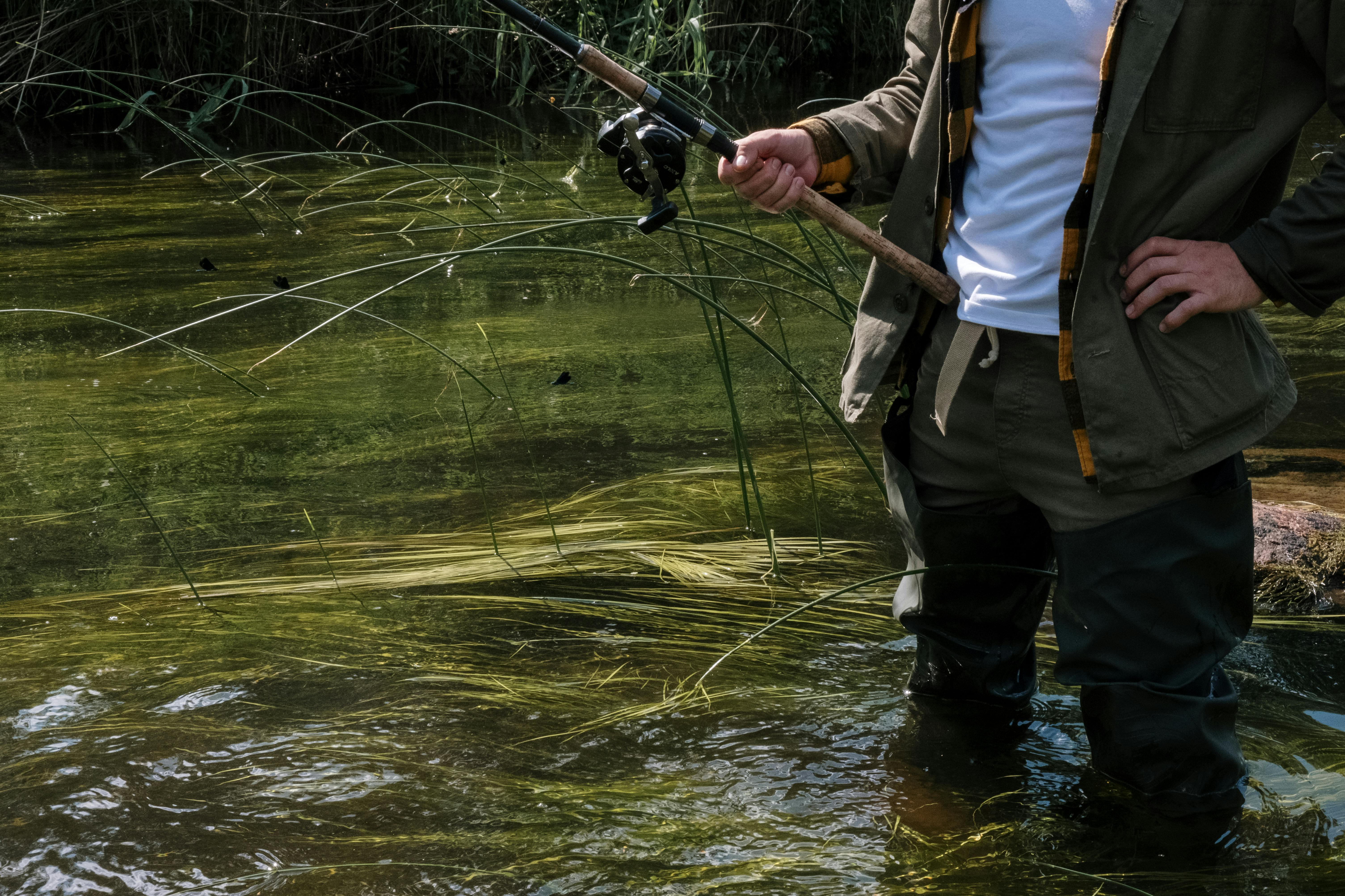 Person beim Angeln im flachen Wasser, mit Angelausrüstung inmitten einer malerischen Naturlandschaft.