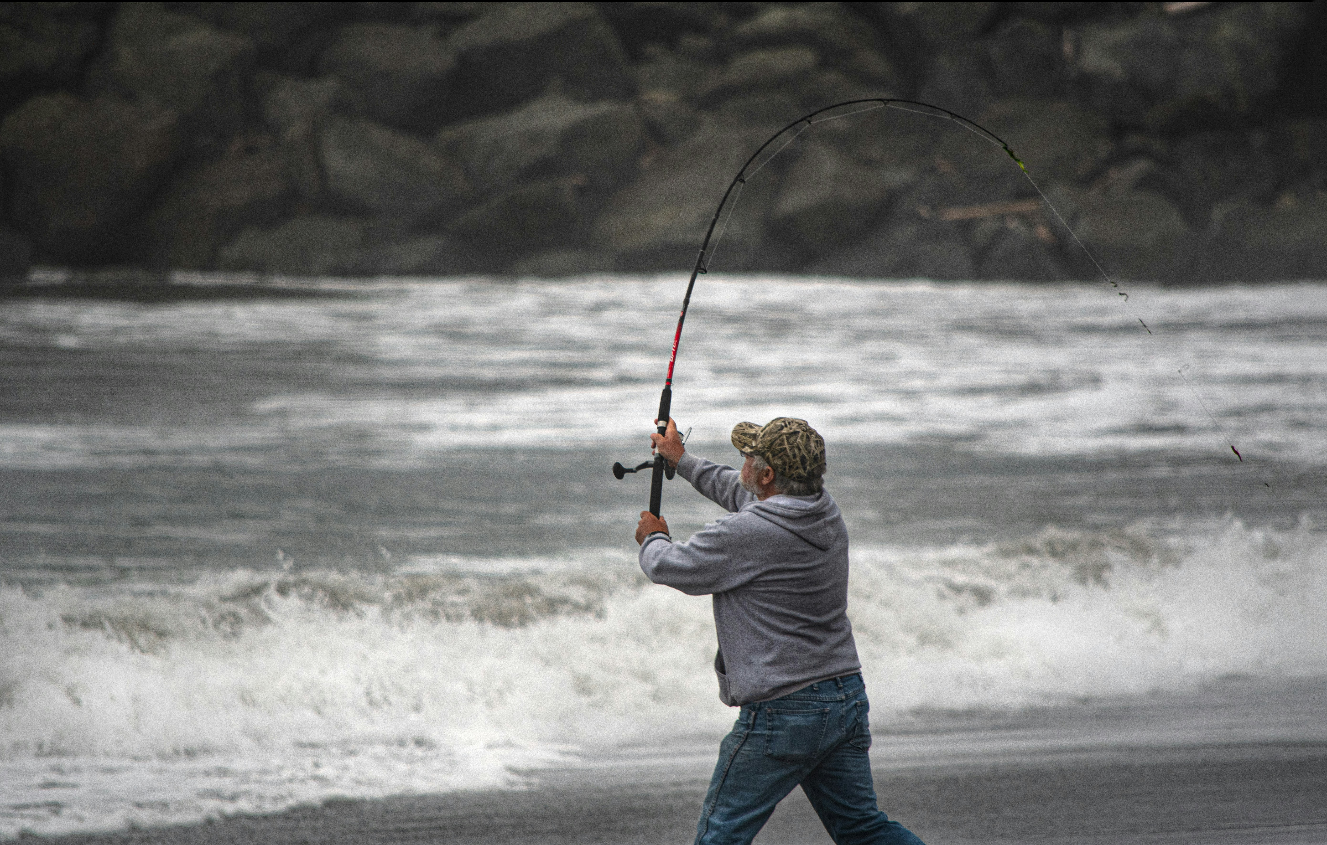 Man fishing on a rugged beach, showcasing fishing gear against a serene ocean backdrop.