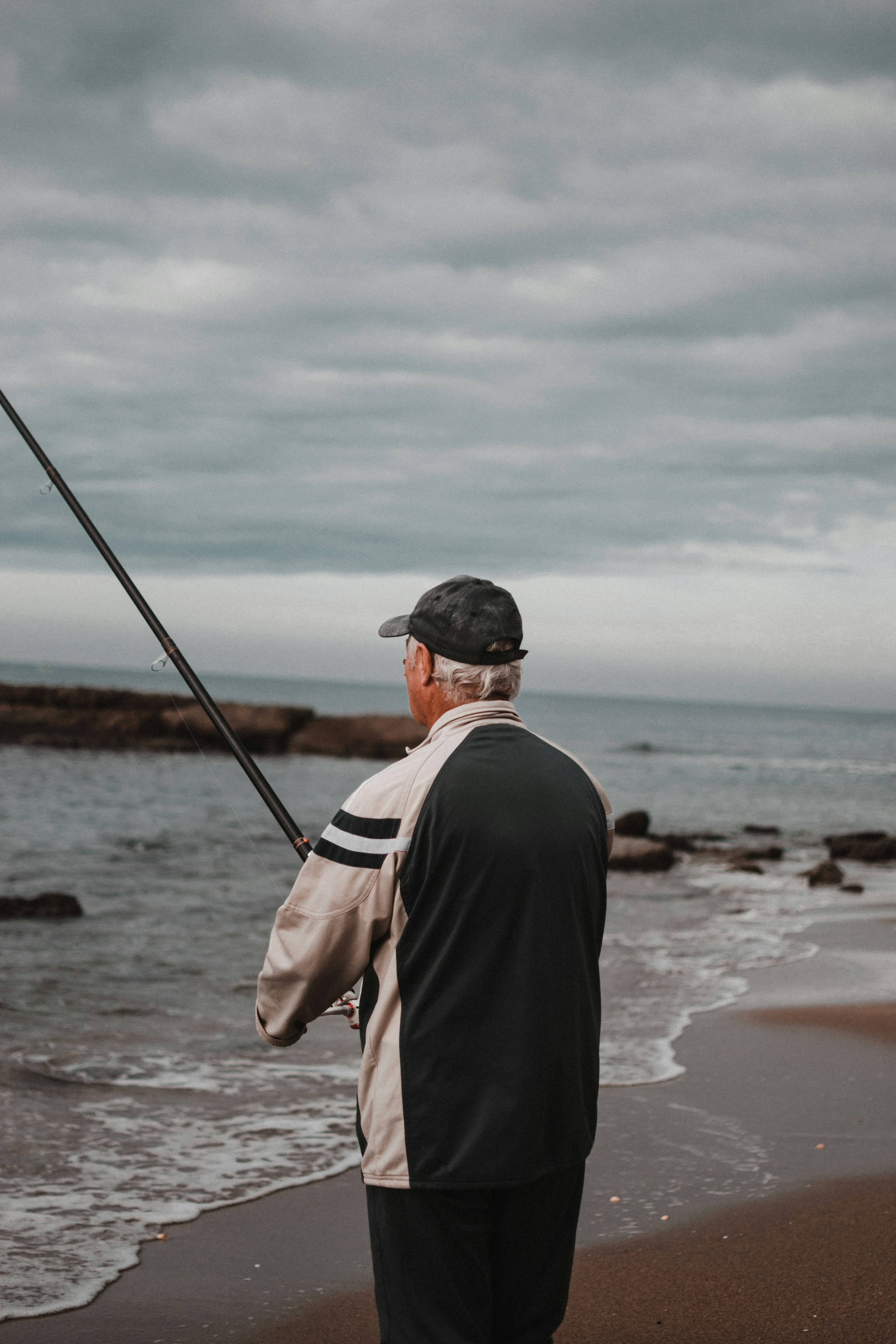 Elderly man fishing on a tranquil beach, showcasing fishing gear amid serene coastal scenery.