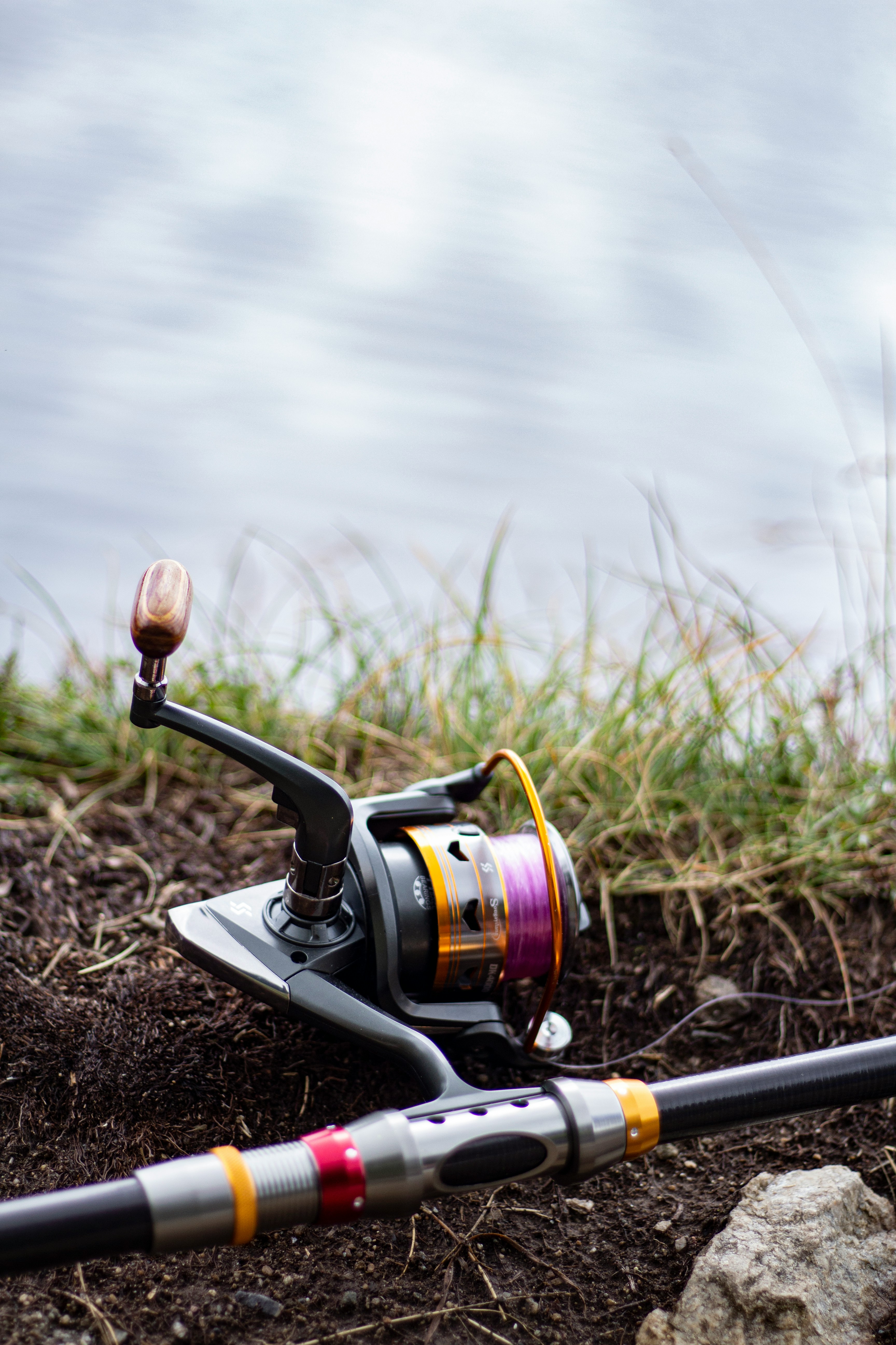 Fishing reel and rod on grass by tranquil water, showcasing quality fishing gear.