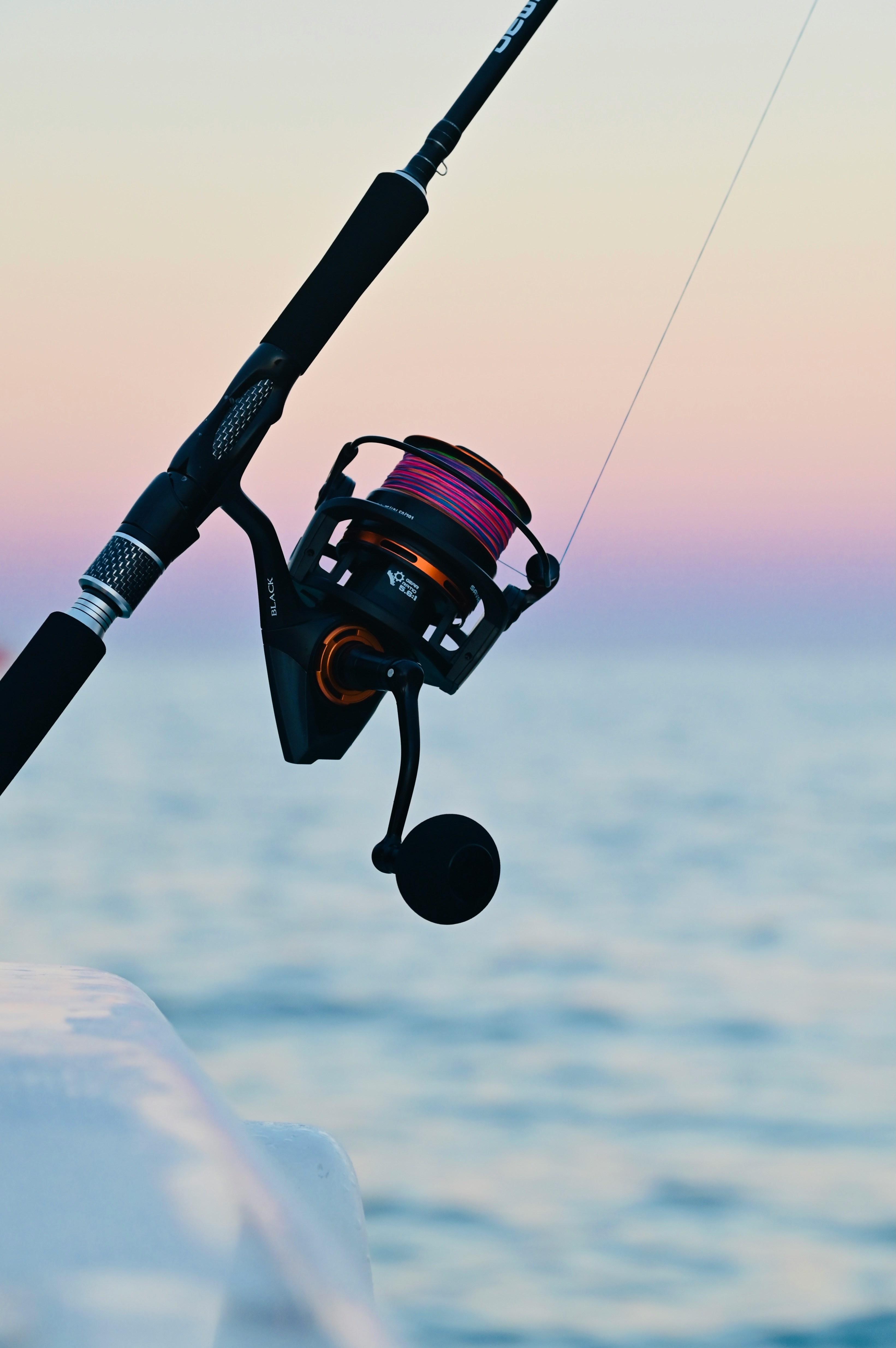 Fishing rod and reel at sunset, showcasing vibrant line against a calm ocean backdrop.