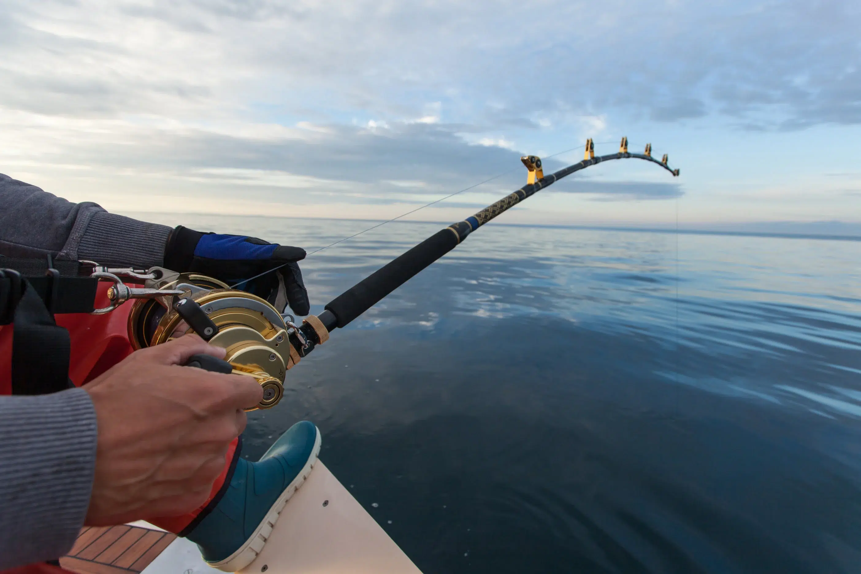 Fisherman with premium fishing rod at sunset, enjoying tranquil angling moments on calm water.