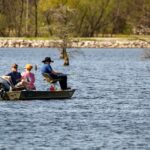 Fishing trip on a spring lake with a serene boat, anglers, and vibrant nature scenery.