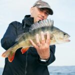 Man proudly displays a large, vibrant fish from a successful fishing trip outdoors.