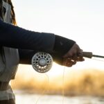 Experienced angler fly fishing at sunrise, showcasing quality fishing gear and peaceful nature.