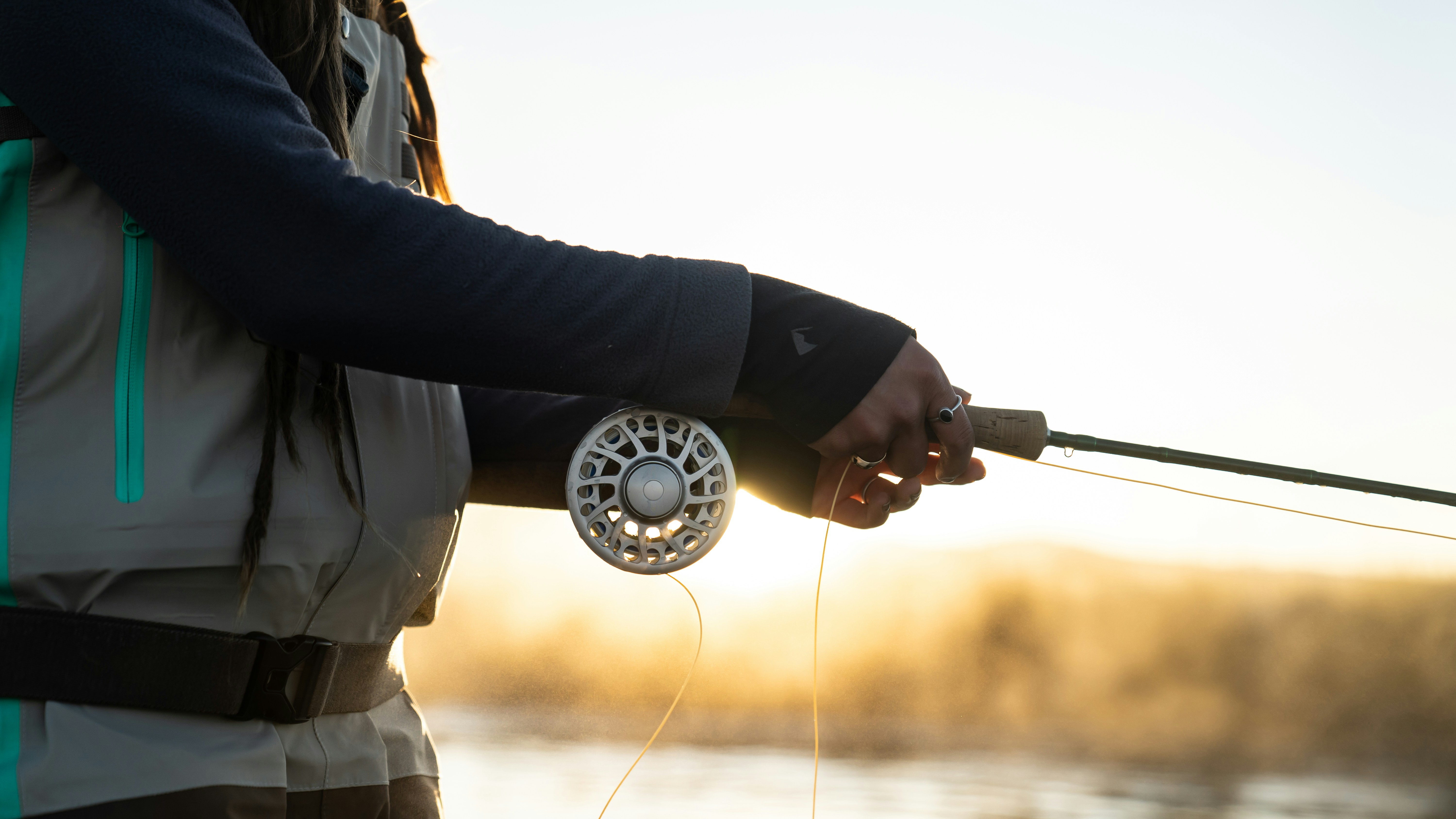 Experienced angler fly fishing at sunrise, showcasing quality fishing gear and peaceful nature.