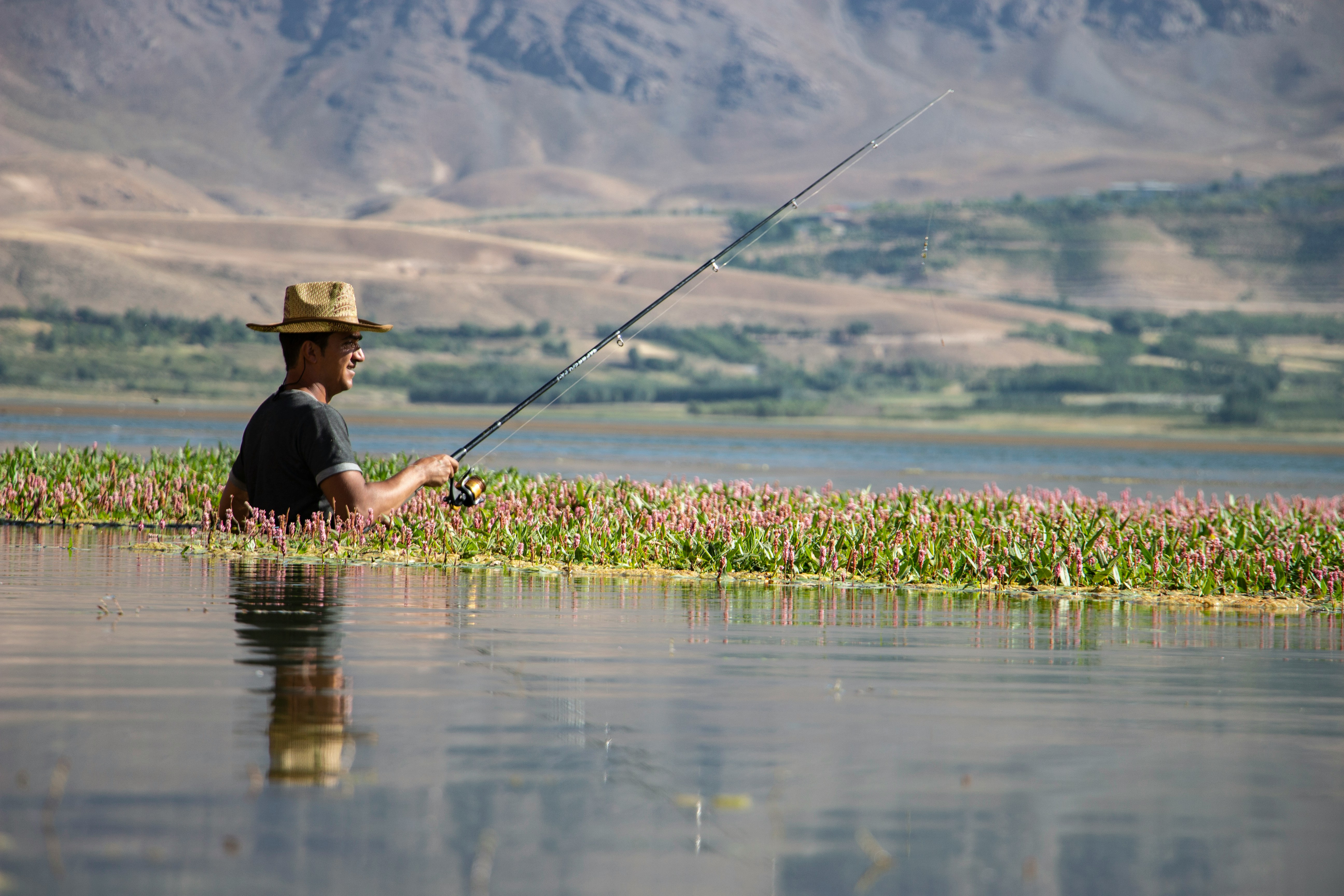 Man fishing in a serene lake, enjoying nature with fishing gear and vibrant surroundings.