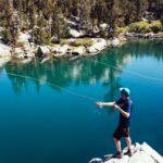 Young man fly fishing in a vibrant lake surrounded by lush nature and clear waters.