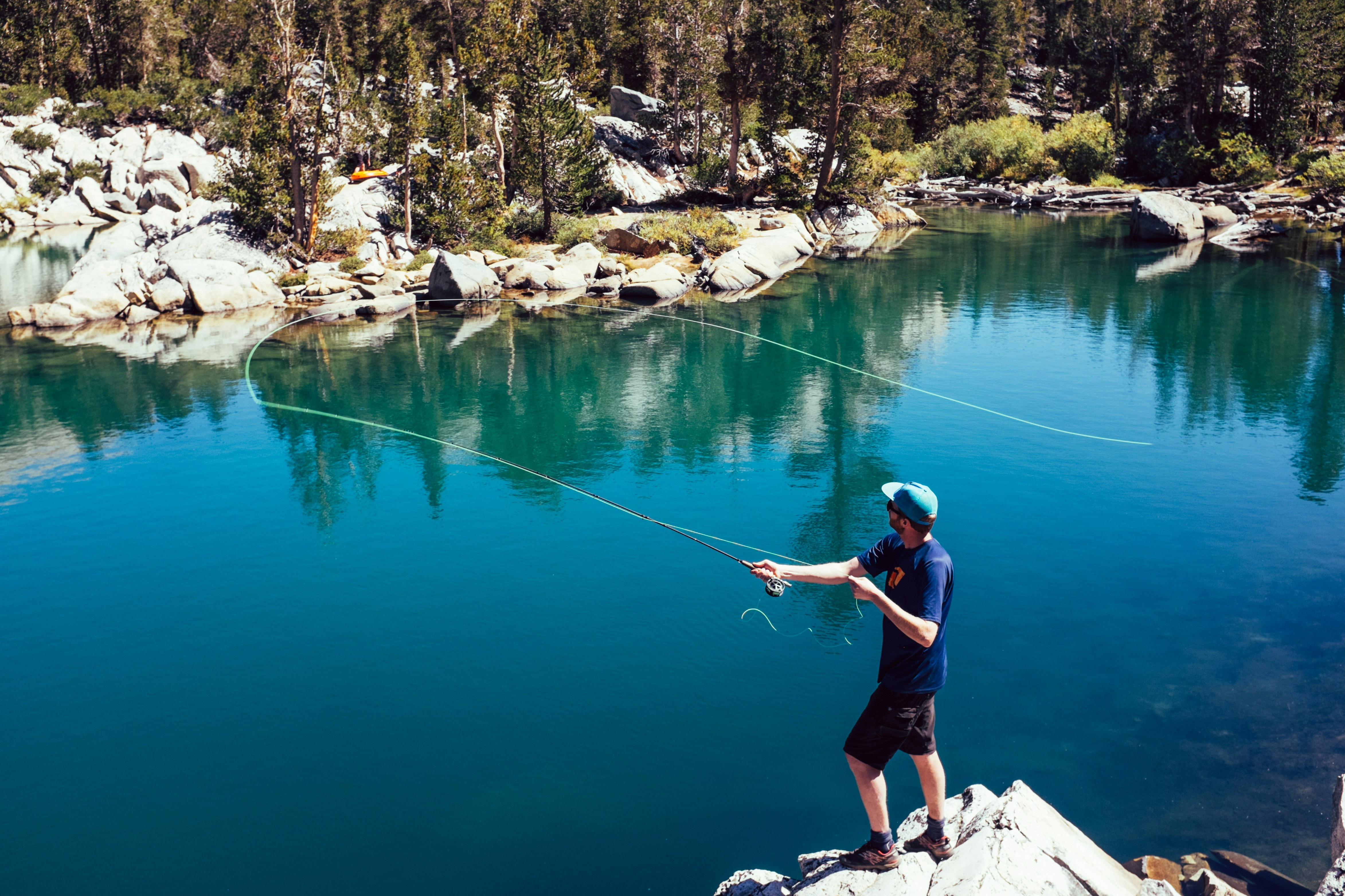 Young man fly fishing in a vibrant lake surrounded by lush nature and clear waters.