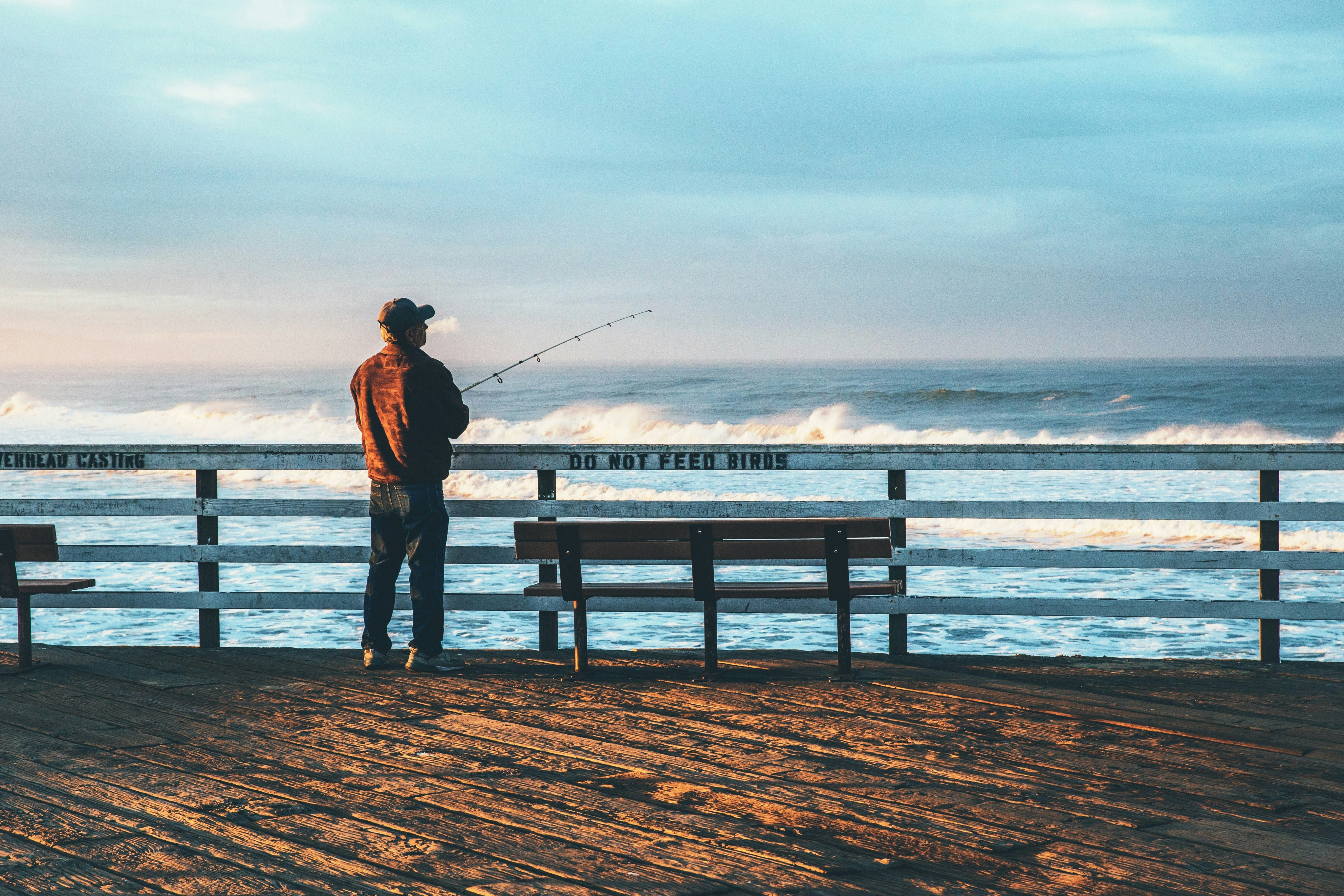 Solitary fisherman on a rustic pier, casting a line into serene ocean waves.