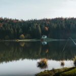 Camouflaged fisherman enjoys peaceful lakeside fishing amidst vibrant autumn colors and serene nature.