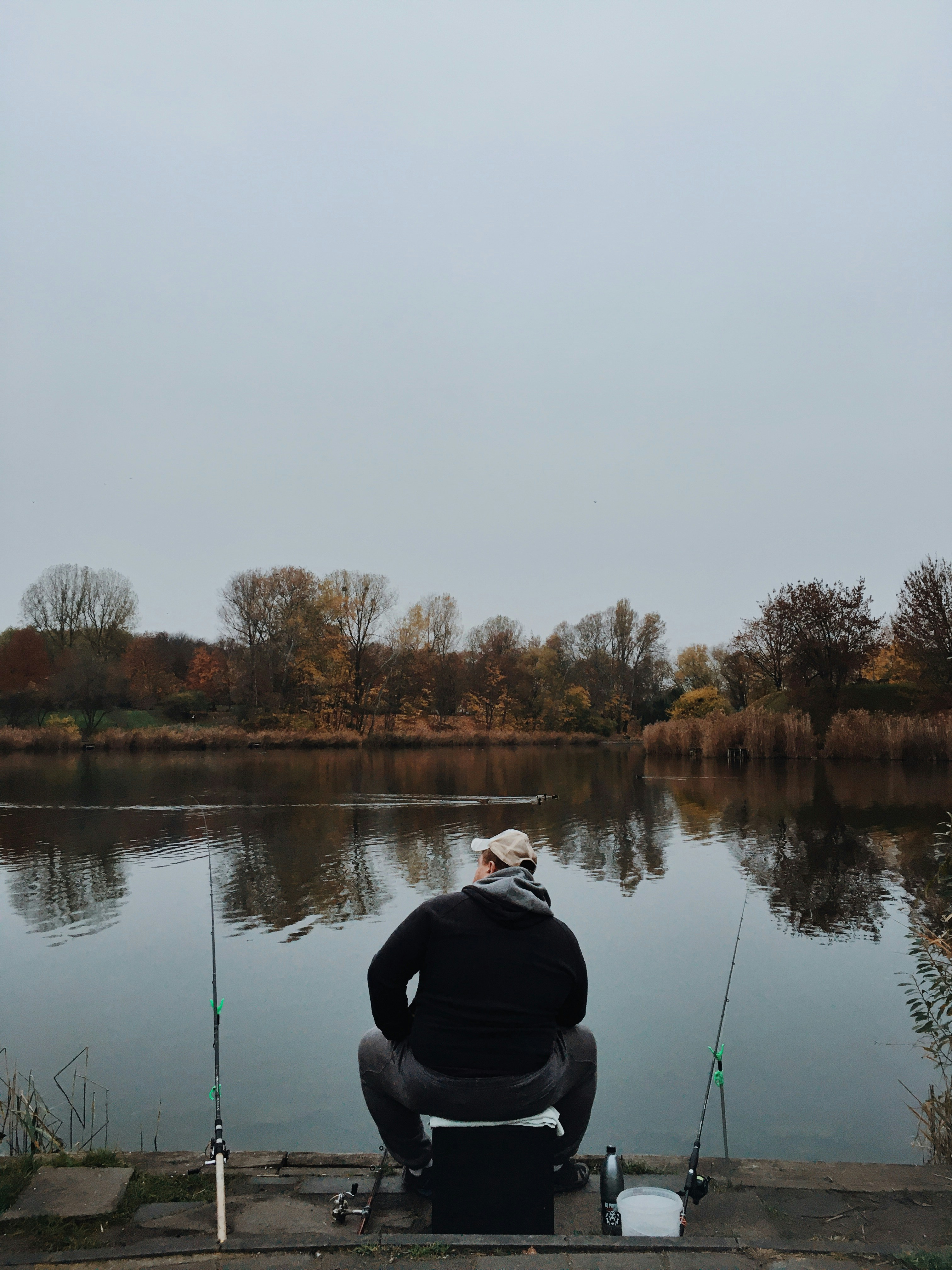 Solitary angler fishing in autumn by tranquil waters, showcasing fishing gear and serene scenery.