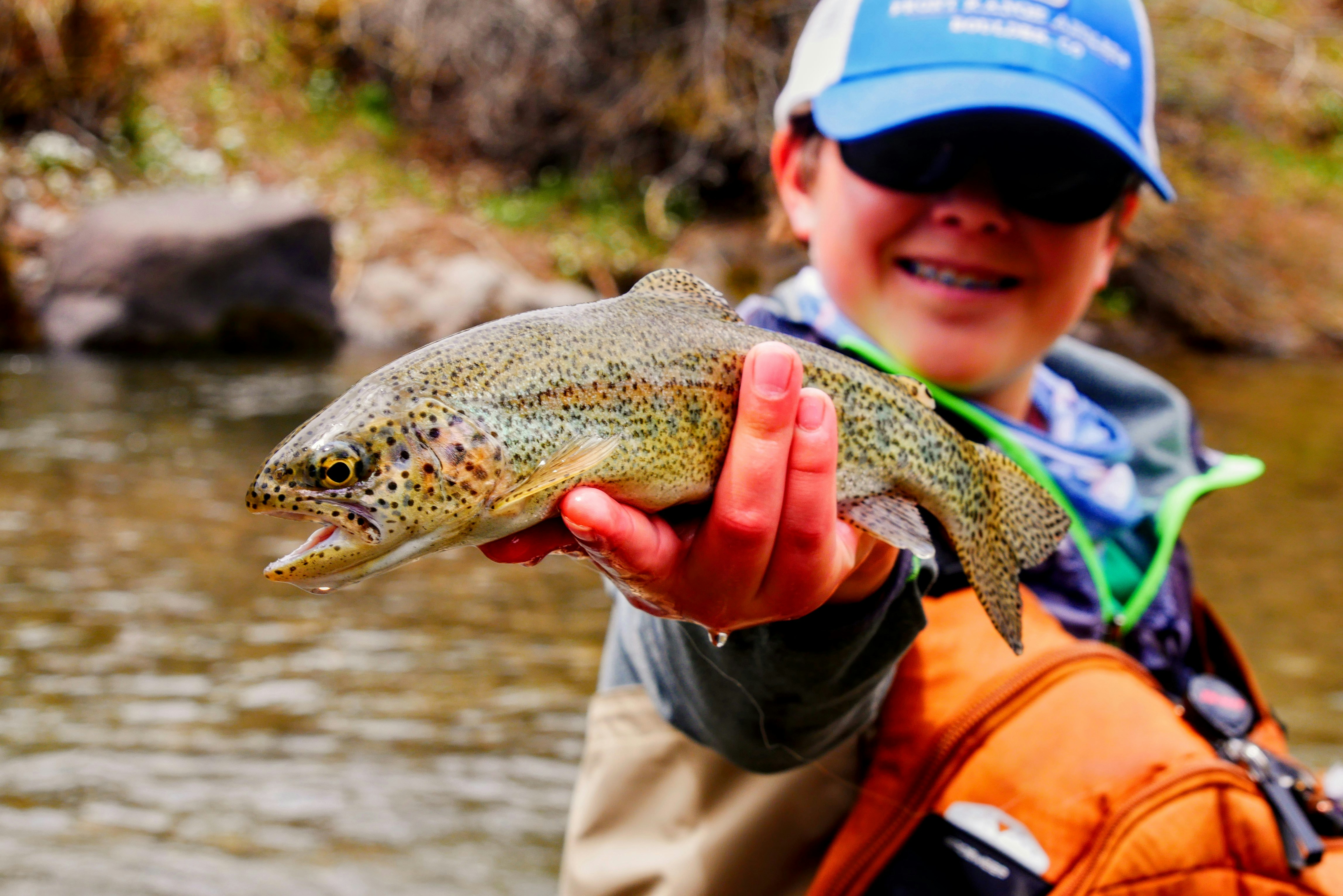 Young boy proudly holding a colorful rainbow trout during a fishing adventure.